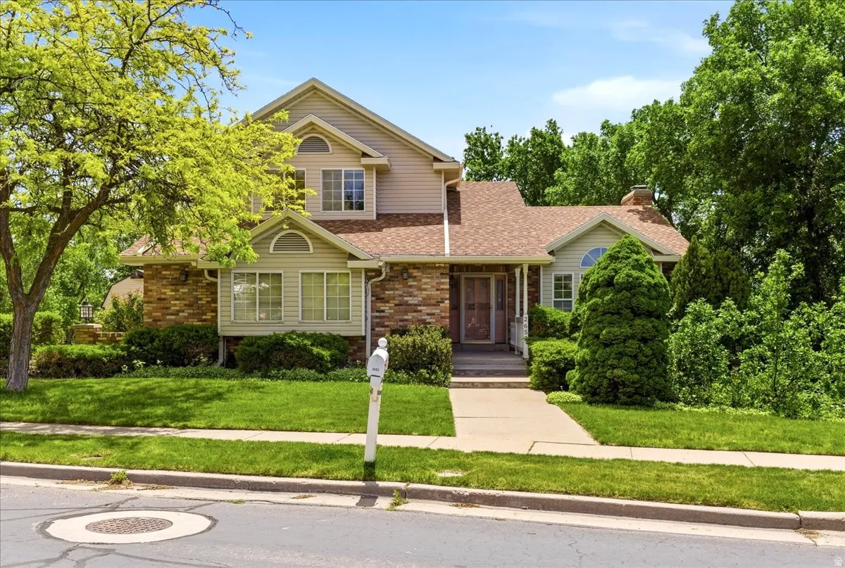 Traditional two-story residence featuring a brick and siding exterior, a front porch entry, an arched window, mature landscaping, and an attached chimney