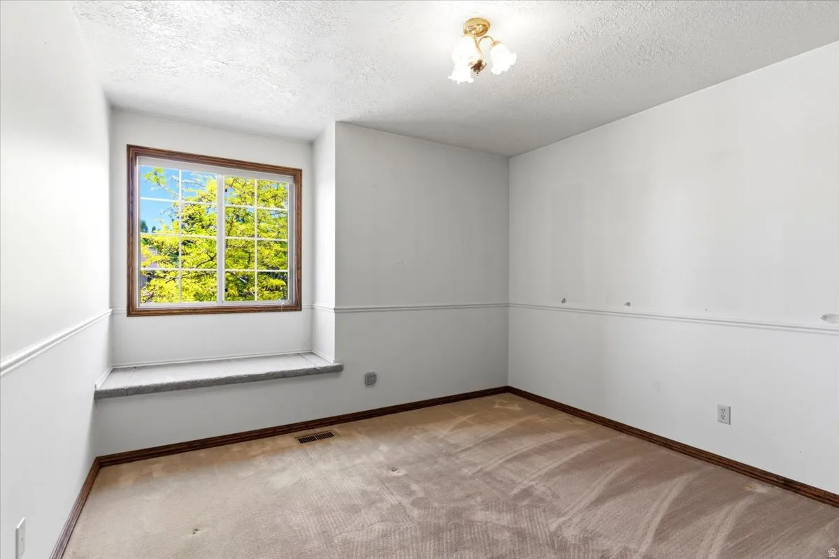 Room featuring a large window with wood-finish trim, a window seat with a textured surface, and a three-light ceiling fixture