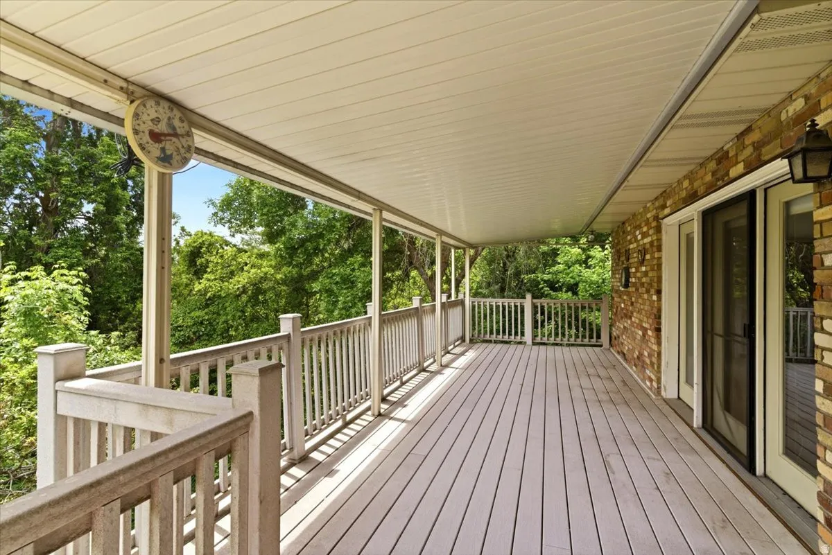 Spacious covered deck featuring composite decking, white railing, and an exposed brick exterior wall