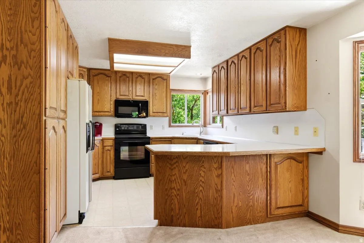 Expansive kitchen featuring abundant wood cabinetry, white countertops, black appliances, and a built-in breakfast bar