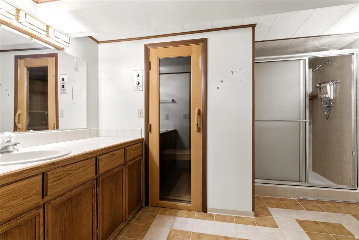 Bathroom featuring a wood-finish vanity with an integrated sink and white countertop, a mirrored wall, a glass-enclosed shower, and a built-in sauna with a glass door