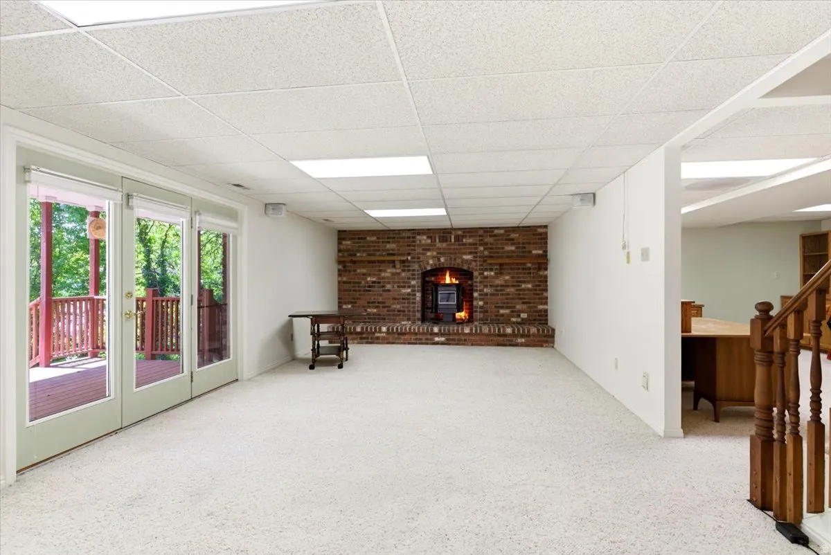 Spacious room featuring a brick fireplace with an insert, light-toned carpeting, and a drop ceiling with integrated lighting