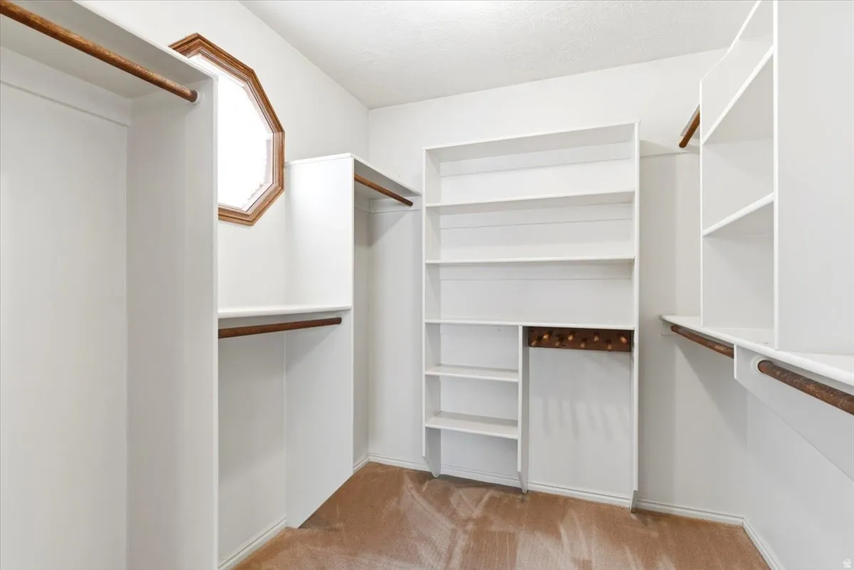 Walk-in closet featuring built-in shelving, hanging rods, and an octagonal window with wood trim