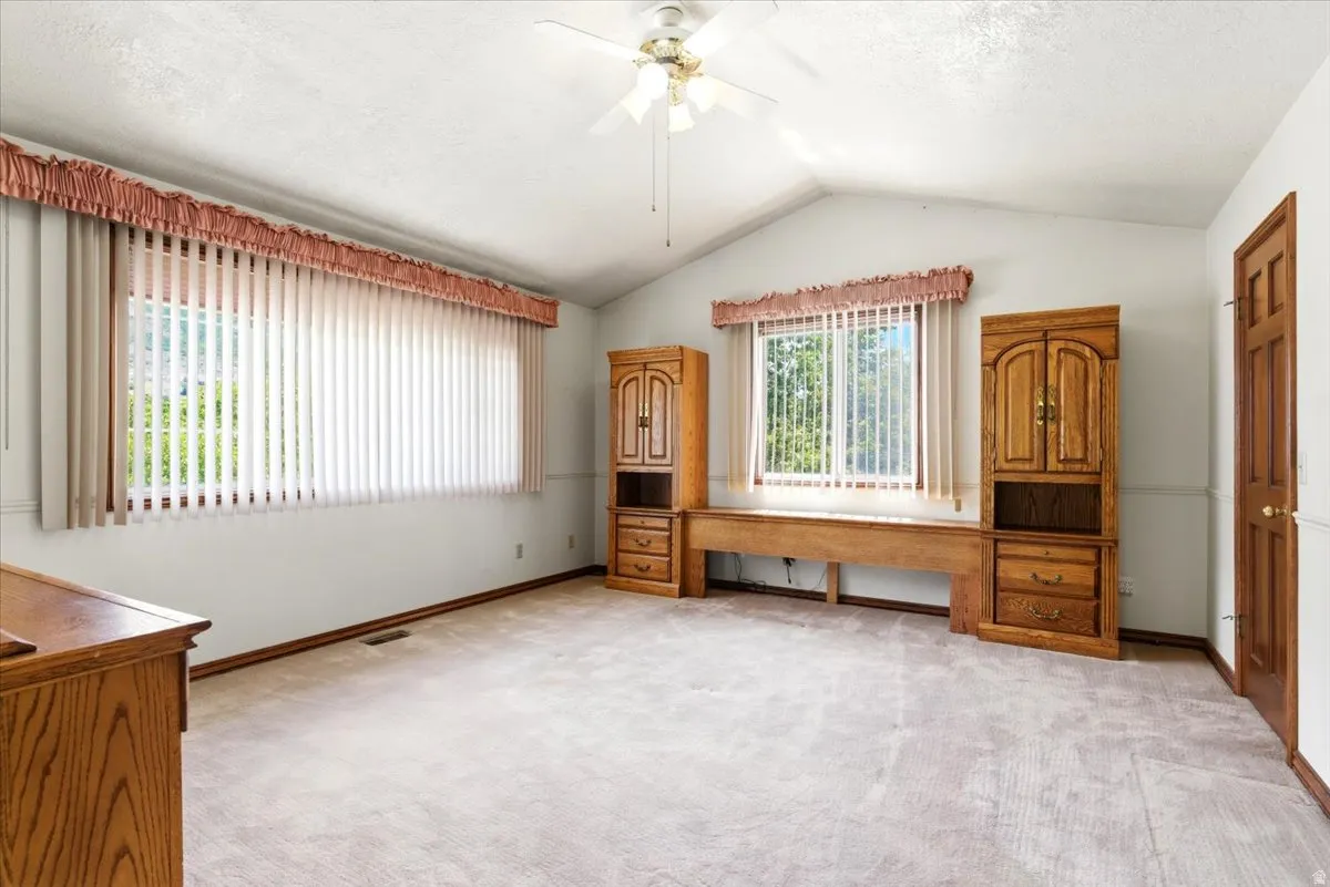 Spacious room featuring vaulted ceilings, light carpeting, and a ceiling fan