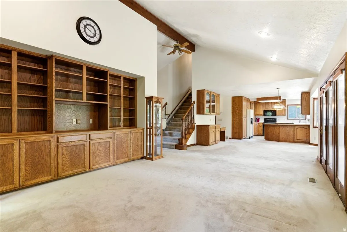 Open-concept interior featuring vaulted ceilings, a built-in entertainment center with extensive wood cabinetry, a staircase with wood railings, recessed lighting, and a kitchen with wood cabinetry and a peninsula