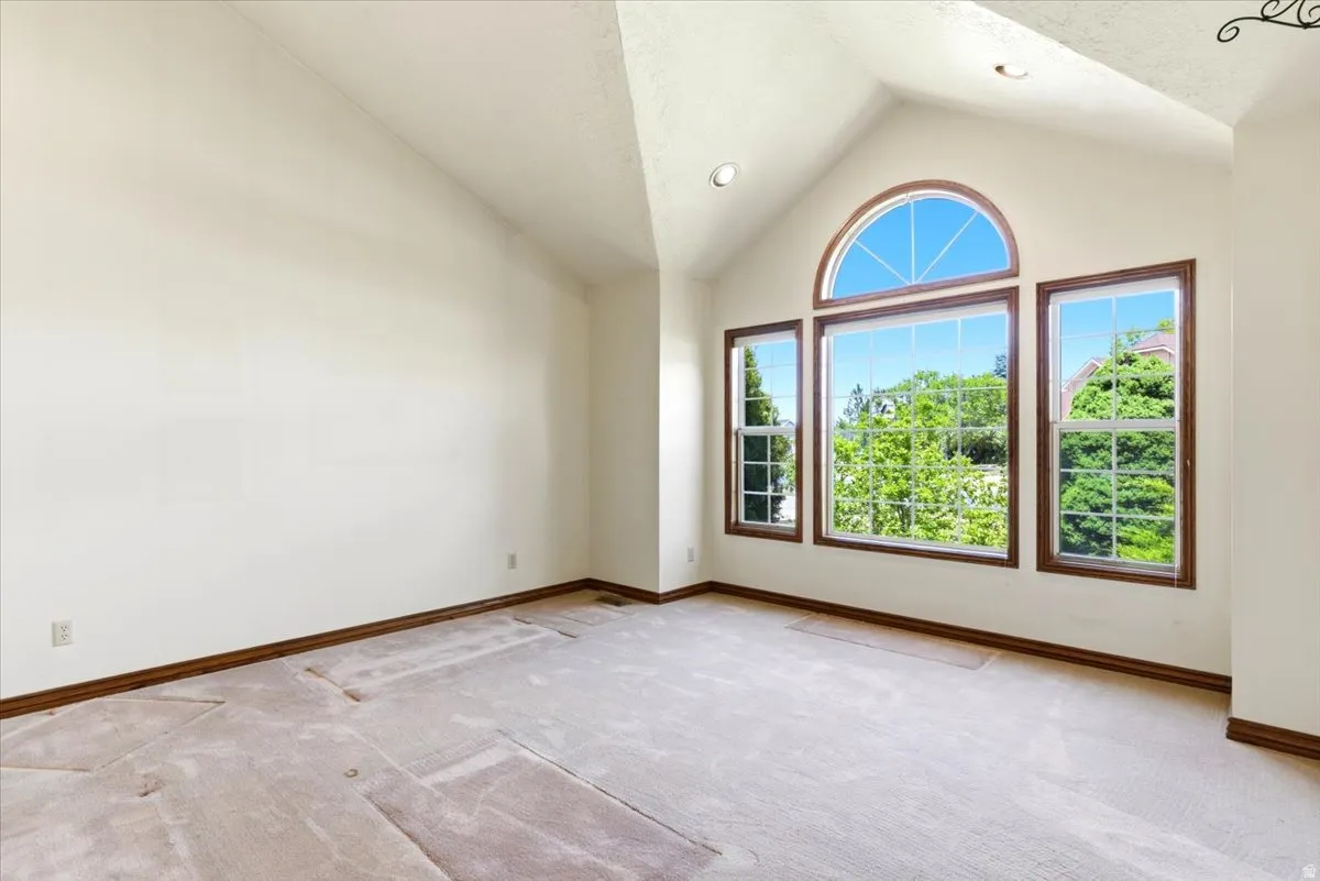 Vaulted ceiling room featuring a large arched window, two additional rectangular windows, recessed lighting, and wood-trim accents