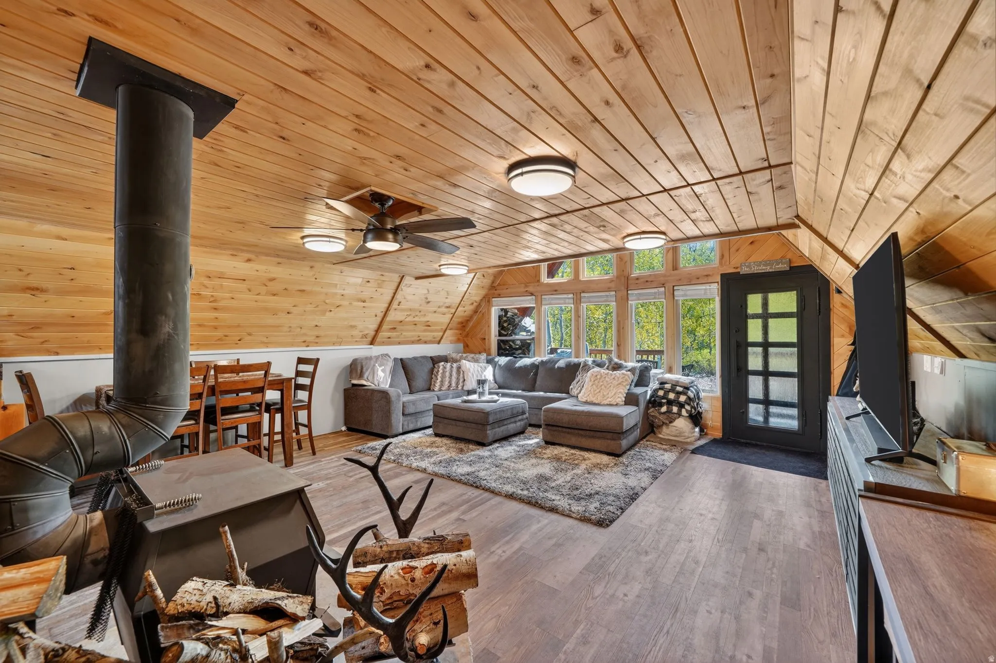 Spacious living area featuring a wood stove, vaulted wood-paneled ceilings, and wood-finish flooring