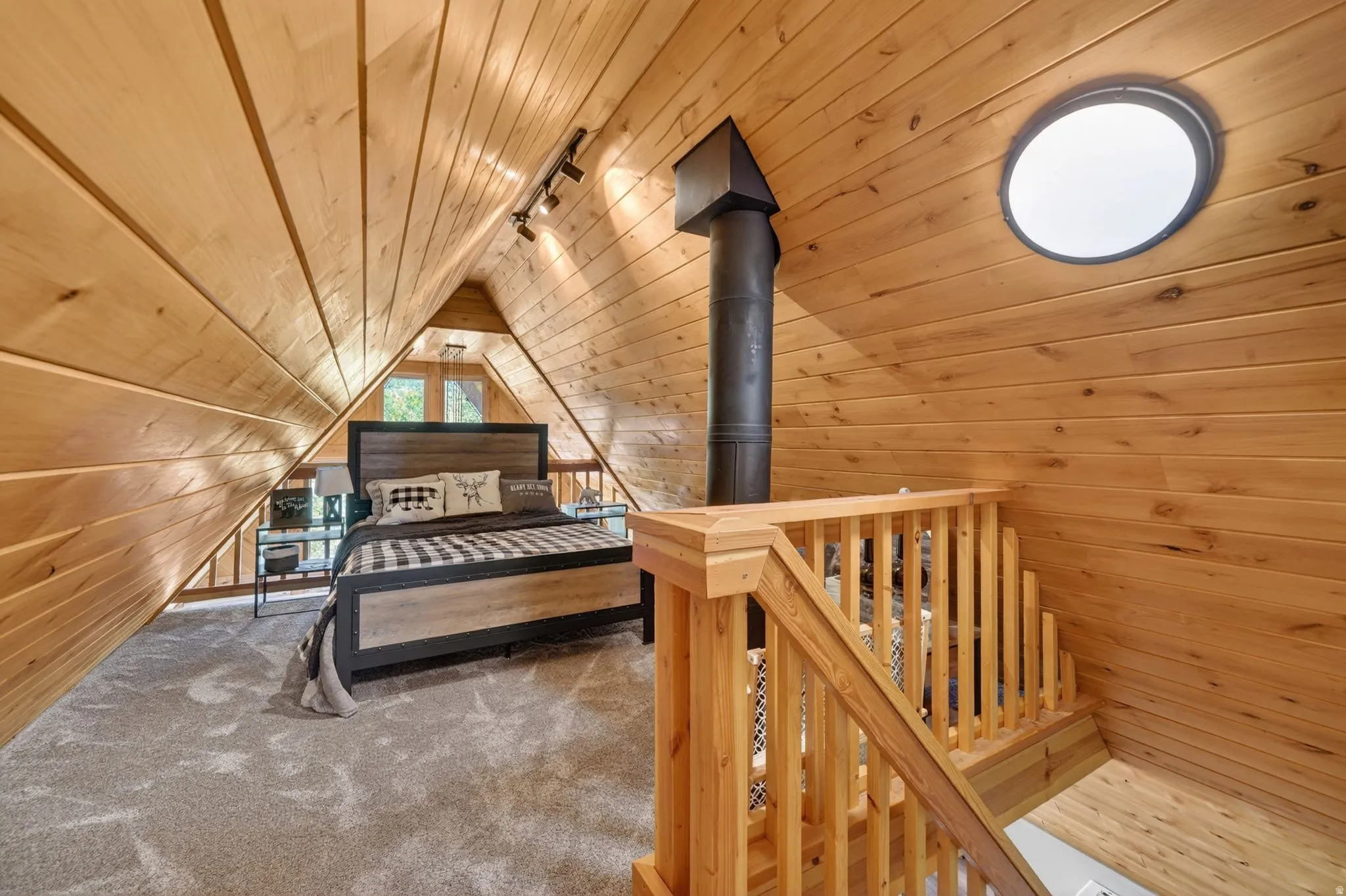 Attic space with wood-finish paneling, a round skylight, track lighting, and a prominent dark stove pipe