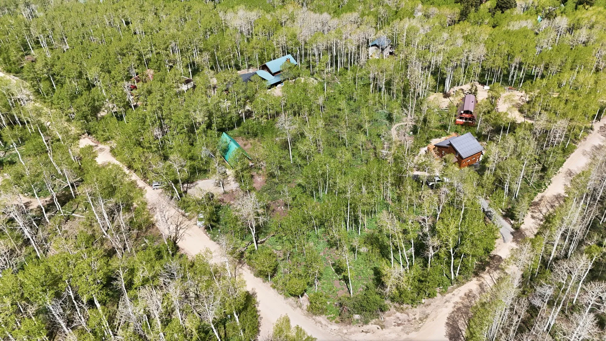 Wooded property with multiple structures featuring brown siding and green or grey roofs