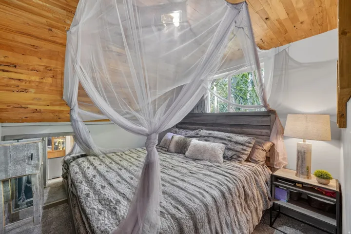 Loft bedroom featuring wood-paneled ceiling, a built-in wood headboard, and a large window