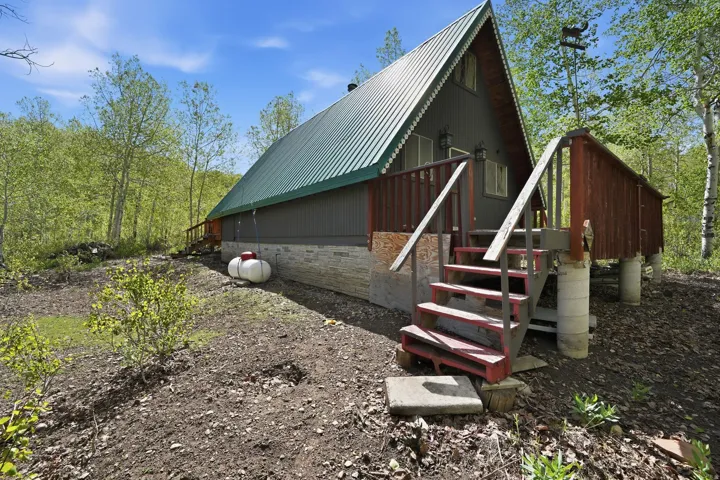 A-frame structure featuring a green metal roof, dark gray corrugated siding, and a stone-clad foundation