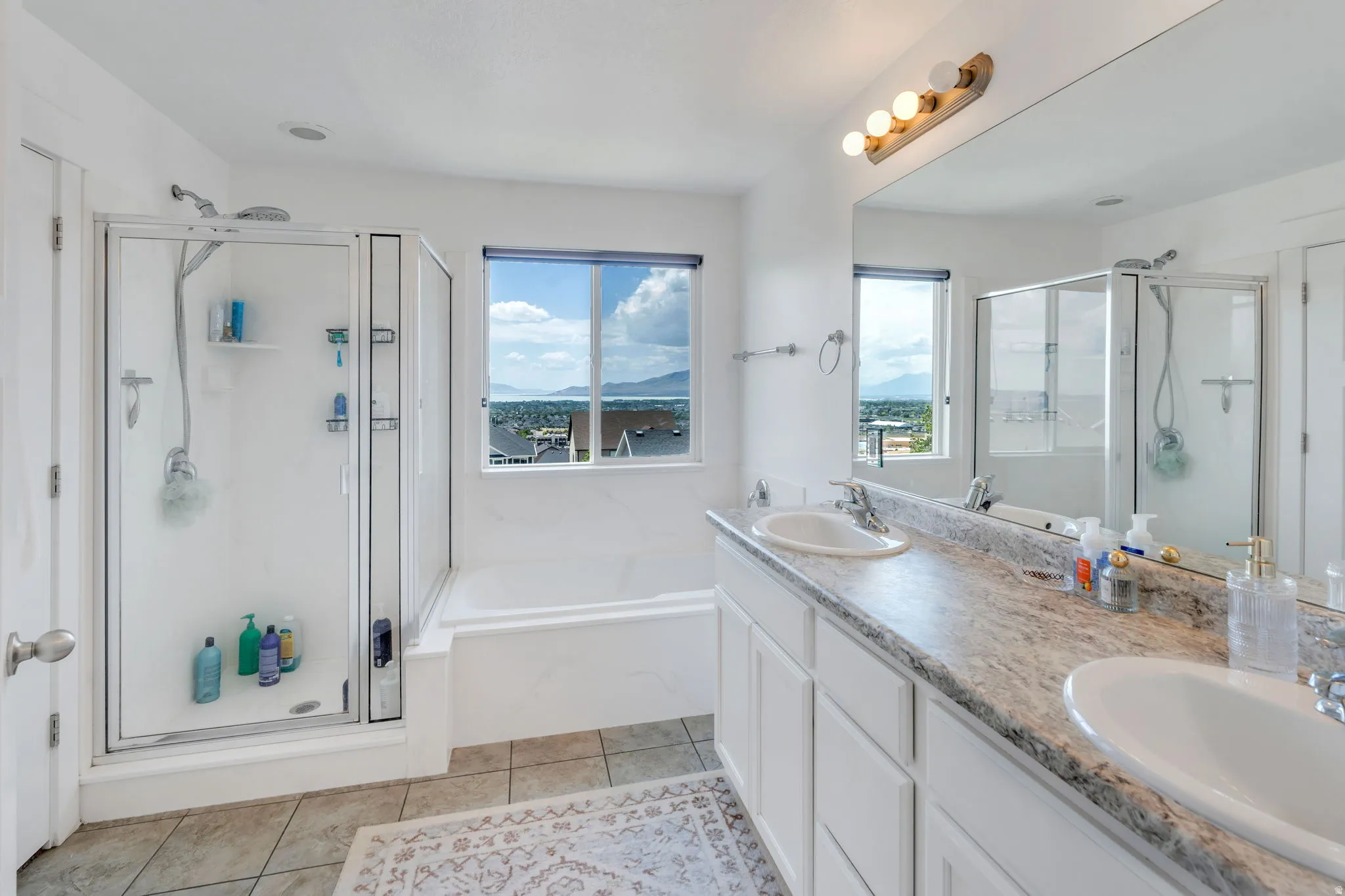 Bathroom featuring a dual-sink vanity with a speckled countertop, a large mirror, and a built-in bathtub