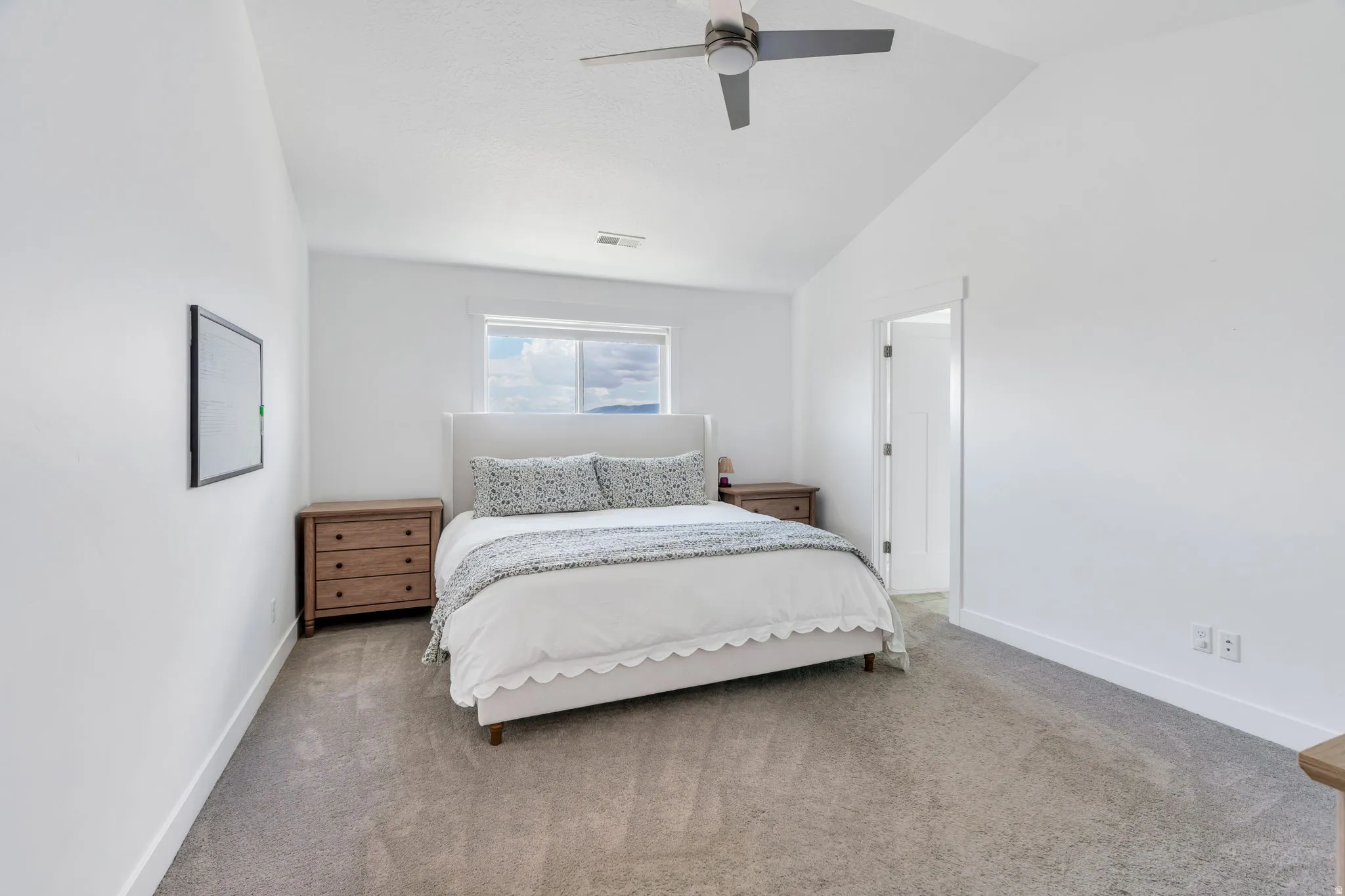 Spacious bedroom featuring vaulted ceilings, a ceiling fan, a window, neutral carpeting, and white baseboards