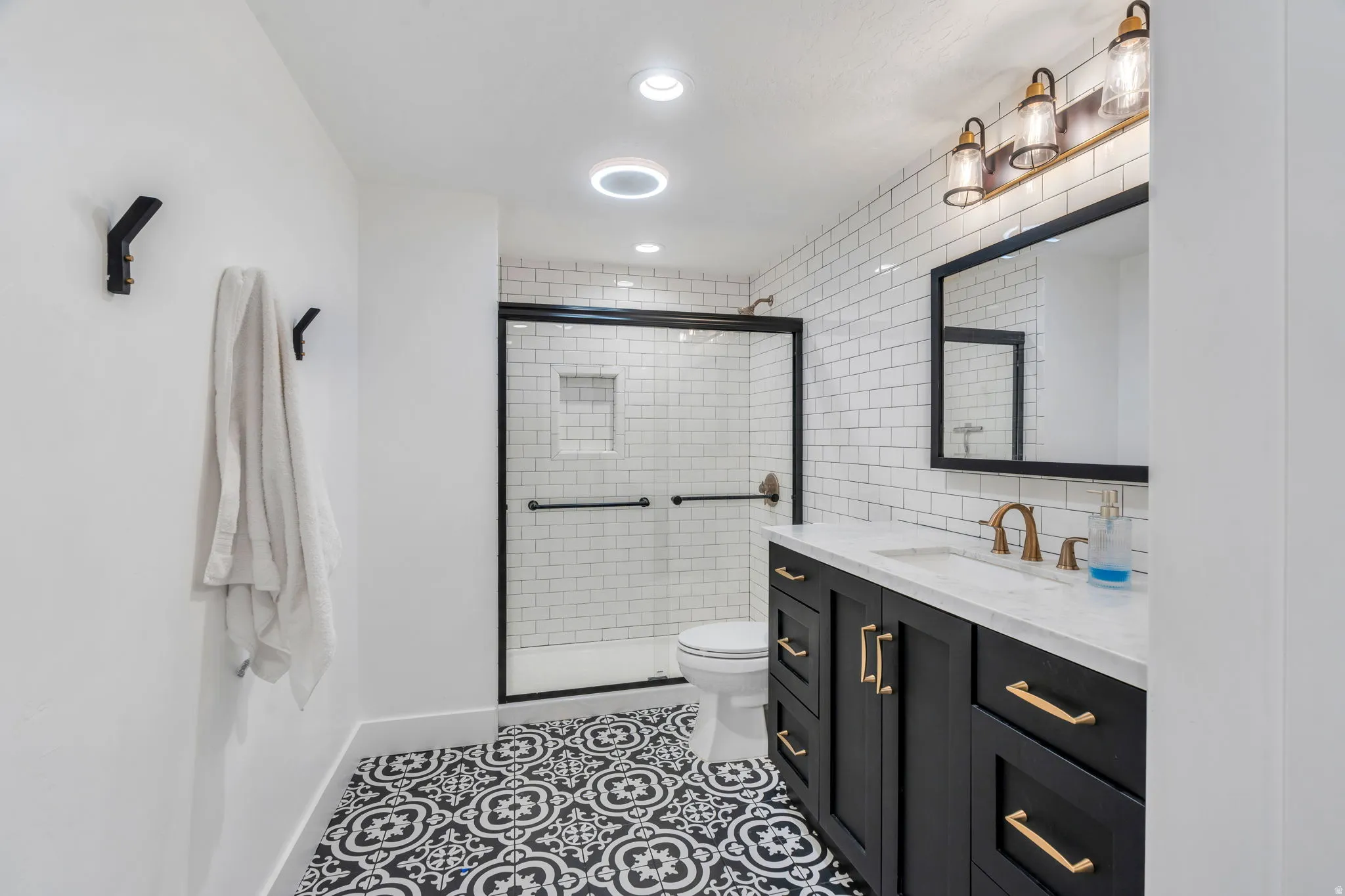 Bathroom featuring a black framed glass shower enclosure, white subway tile shower surround, and a black vanity with a white countertop