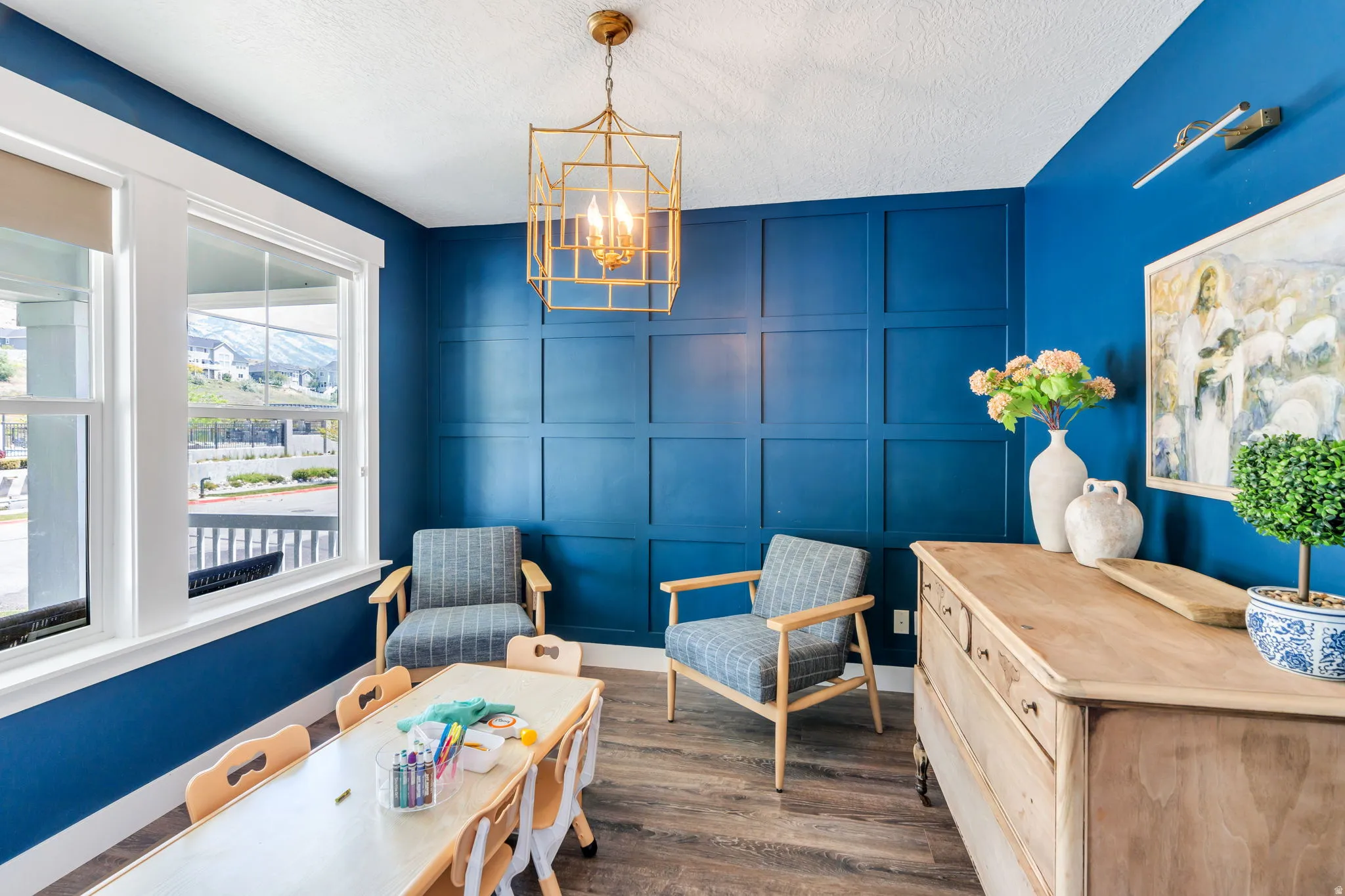Room featuring wood-finish flooring, a decorative wall panel accent, and a gold-toned geometric chandelier