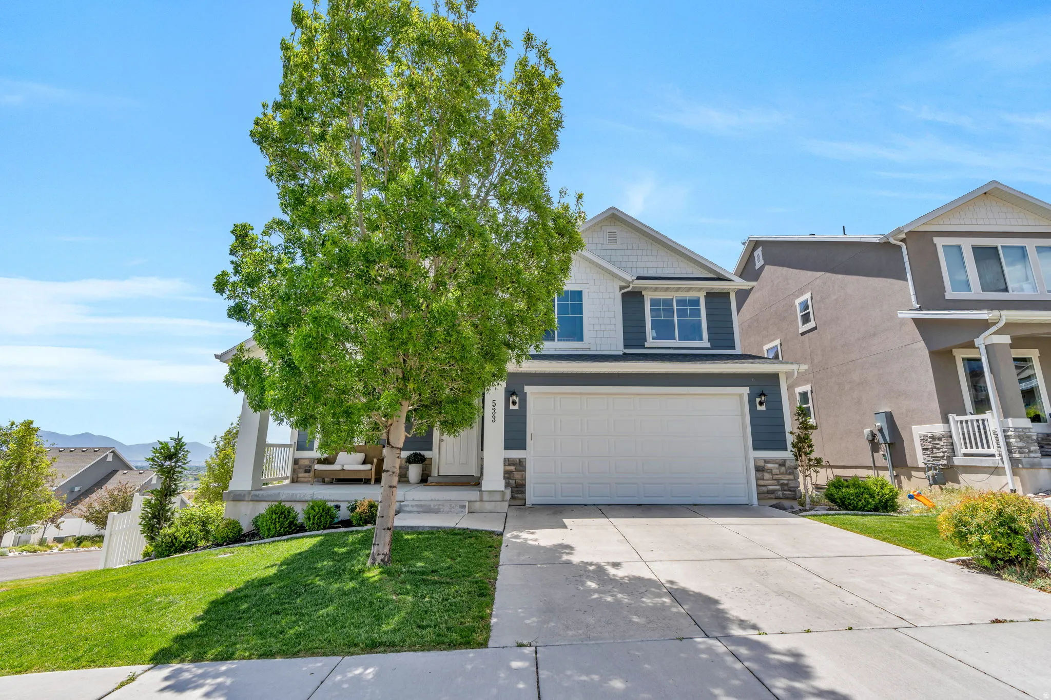 Contemporary two-story residence featuring a two-car garage, partial stone facade, covered front porch, and a concrete driveway