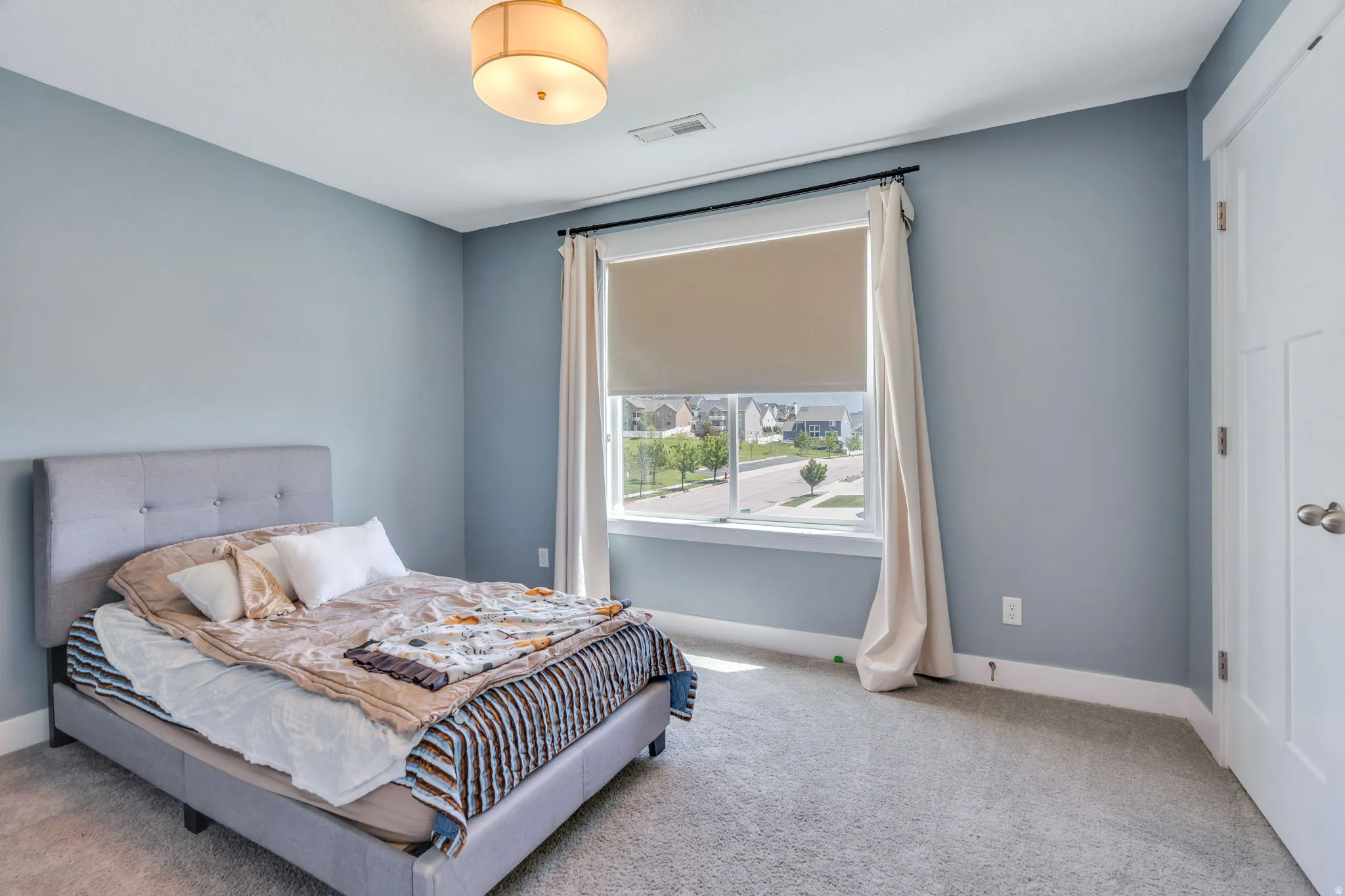 Carpeted room featuring a large window with roller shade, overhead drum light fixture, and white trim and baseboards
