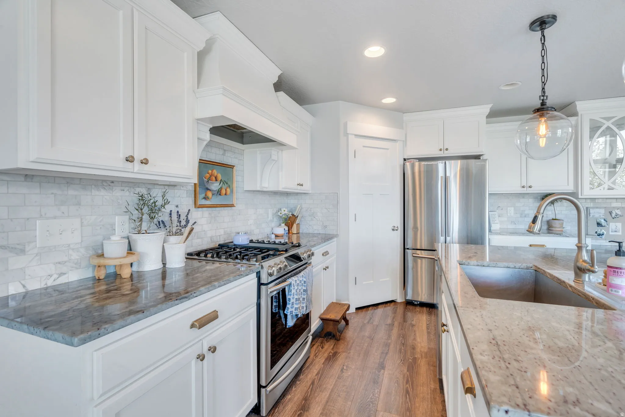 Spacious kitchen featuring white cabinetry, light-toned backsplash, stainless steel appliances, granite countertops, and wood-finish flooring