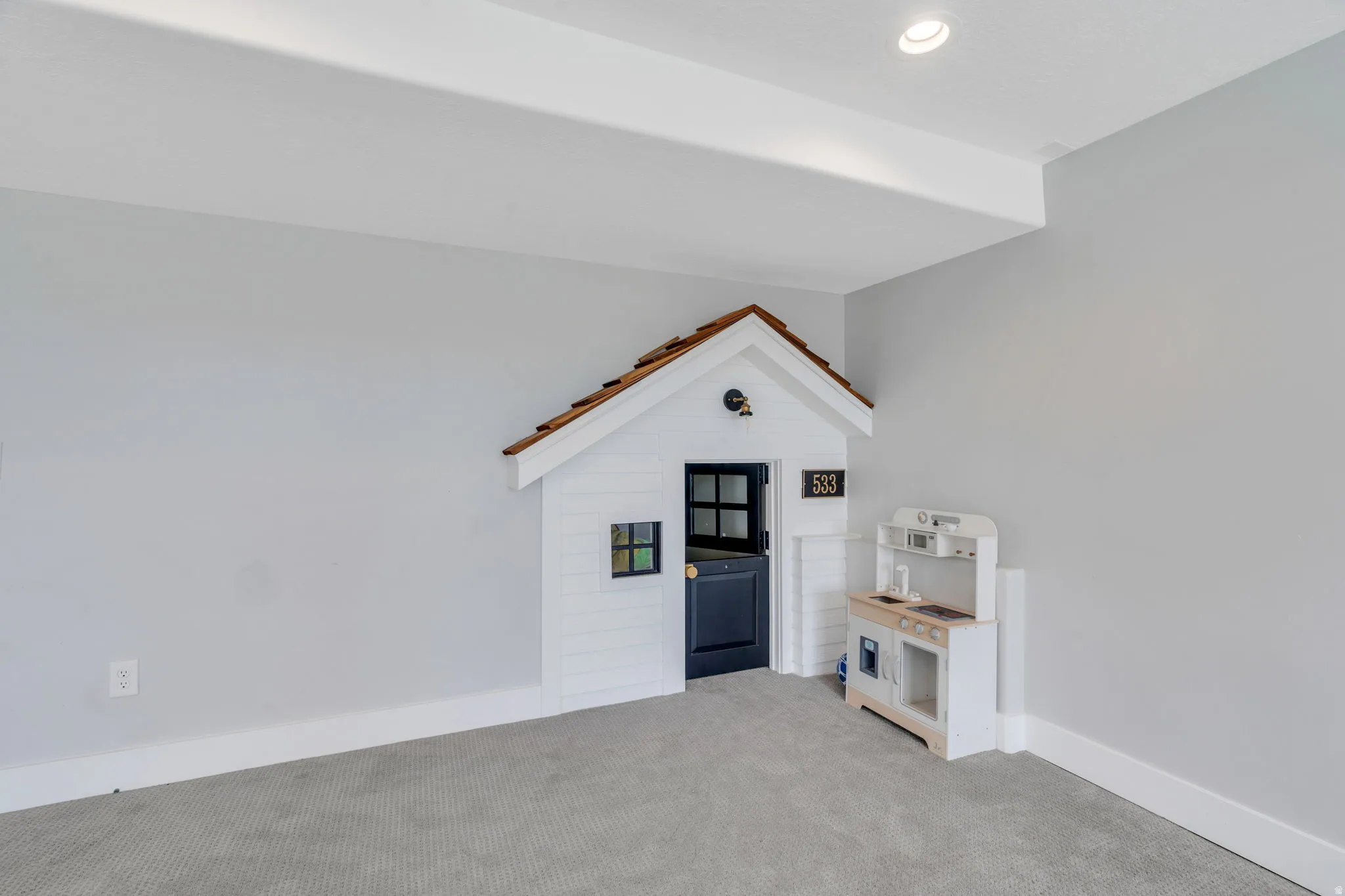 Recessed lighting illuminates a built-in playhouse featuring a shingled roof, a dark paneled door with a brass-colored knob, and a window with dark framing