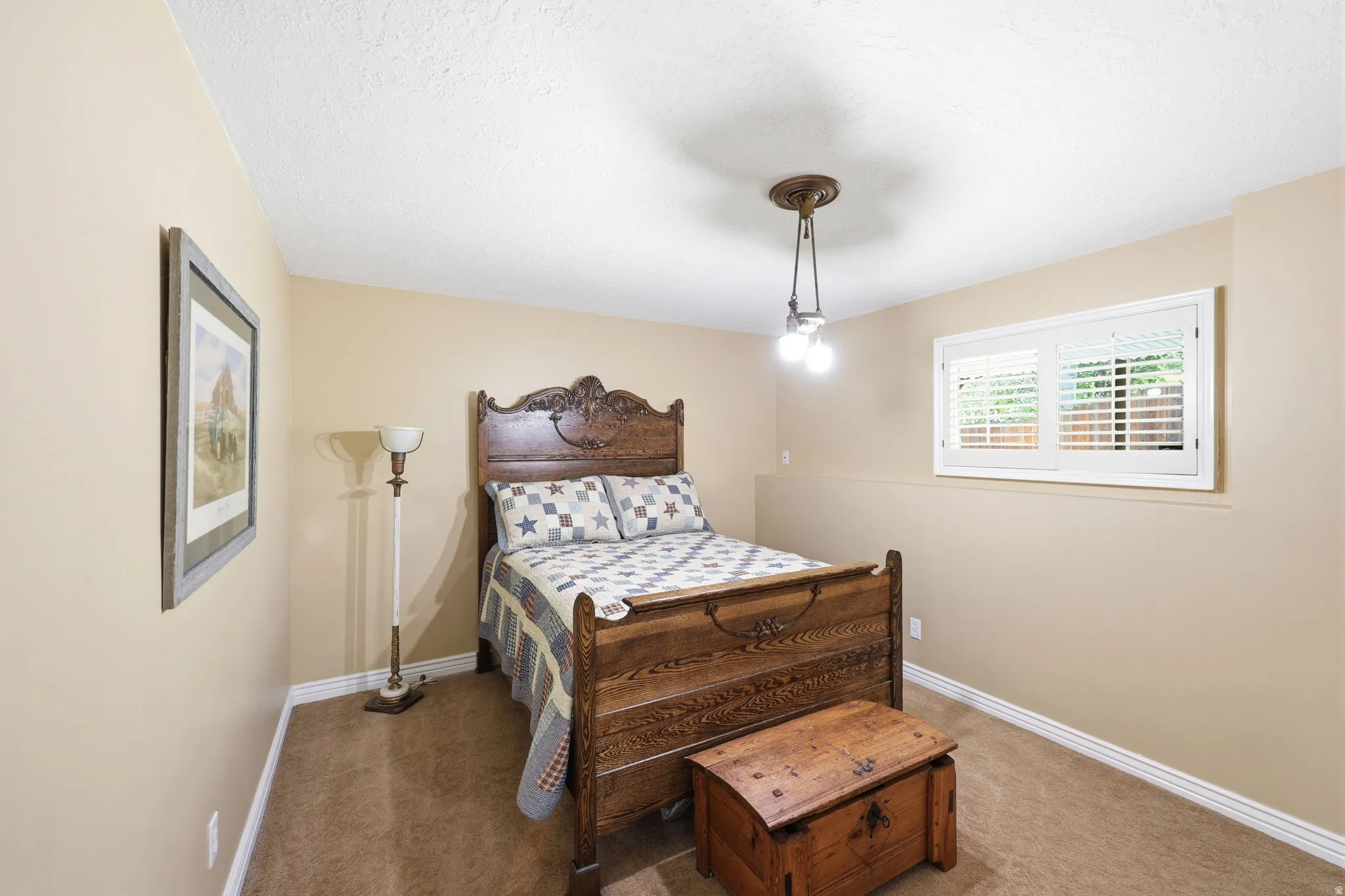 Carpeted room with a ceiling-mounted light fixture and a window featuring white plantation shutters