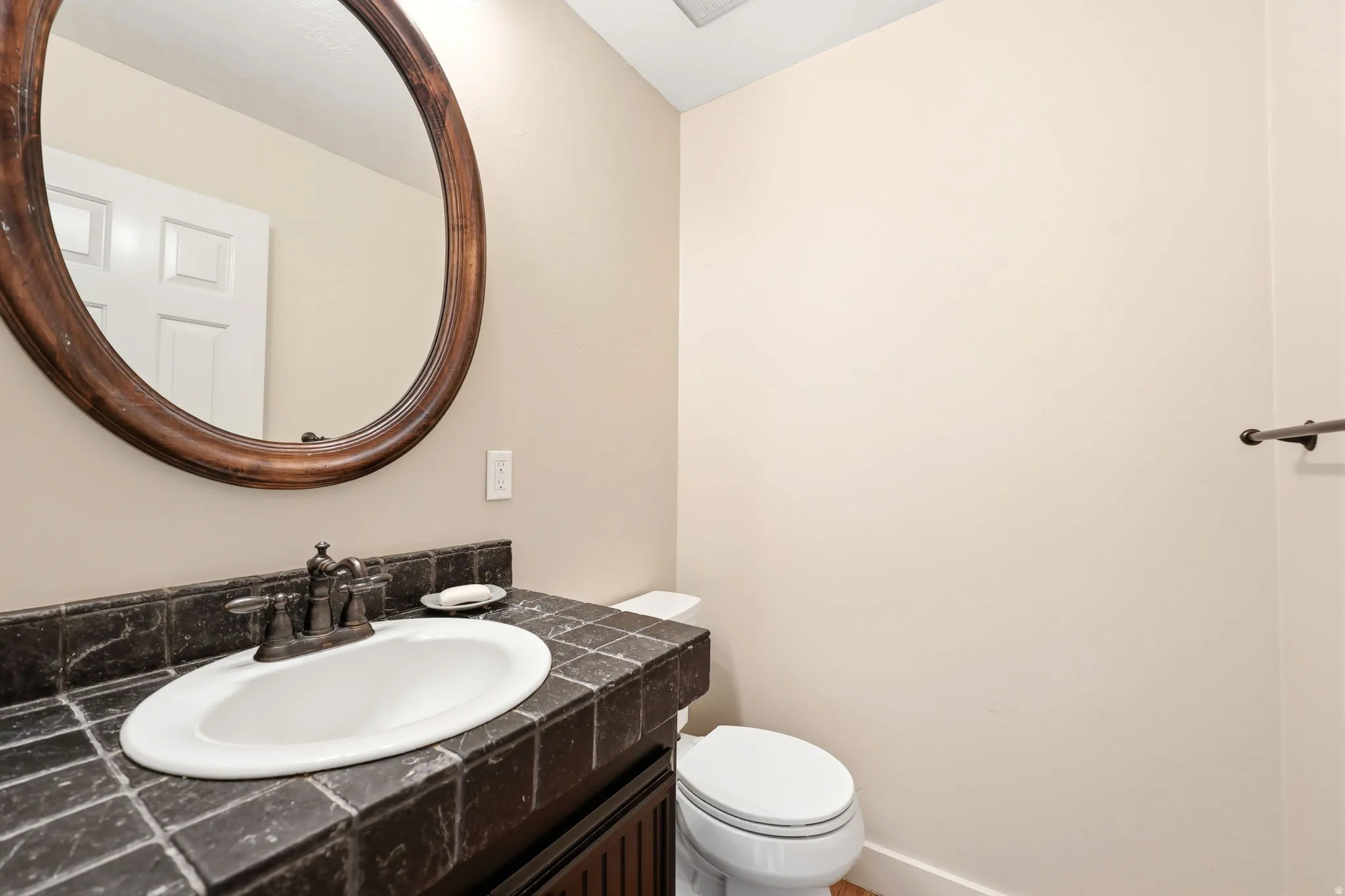 Bathroom featuring a dark tiled countertop, integrated sink, and an oval wood-framed mirror