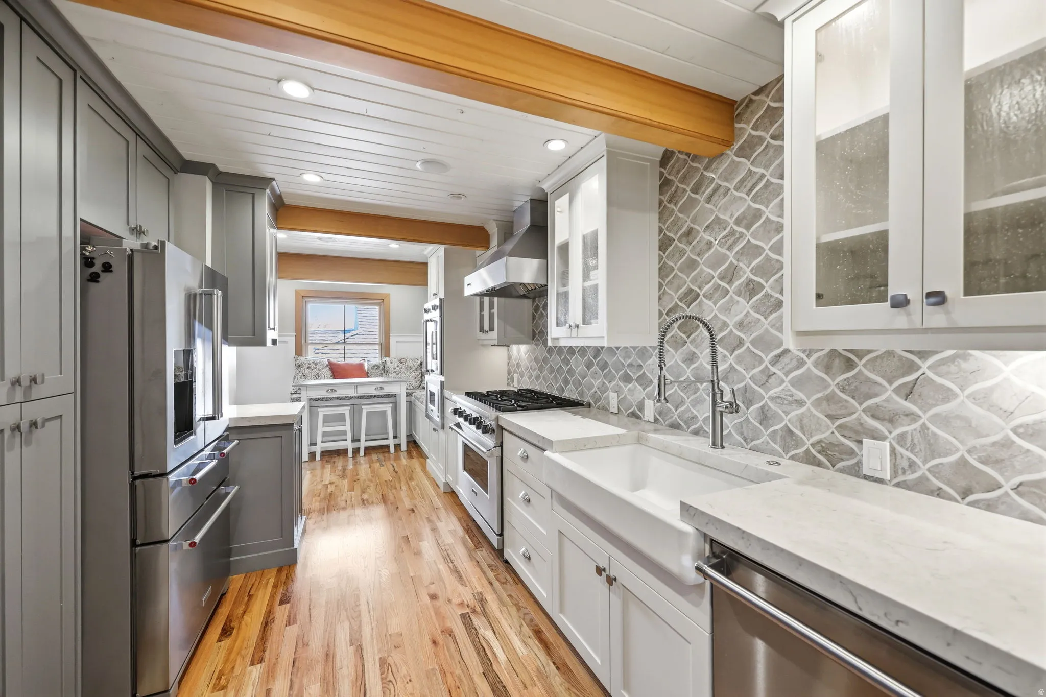 Gourmet kitchen featuring a farmhouse sink, stainless steel appliances, wood-finish flooring, a decorative tile backsplash, and recessed lighting