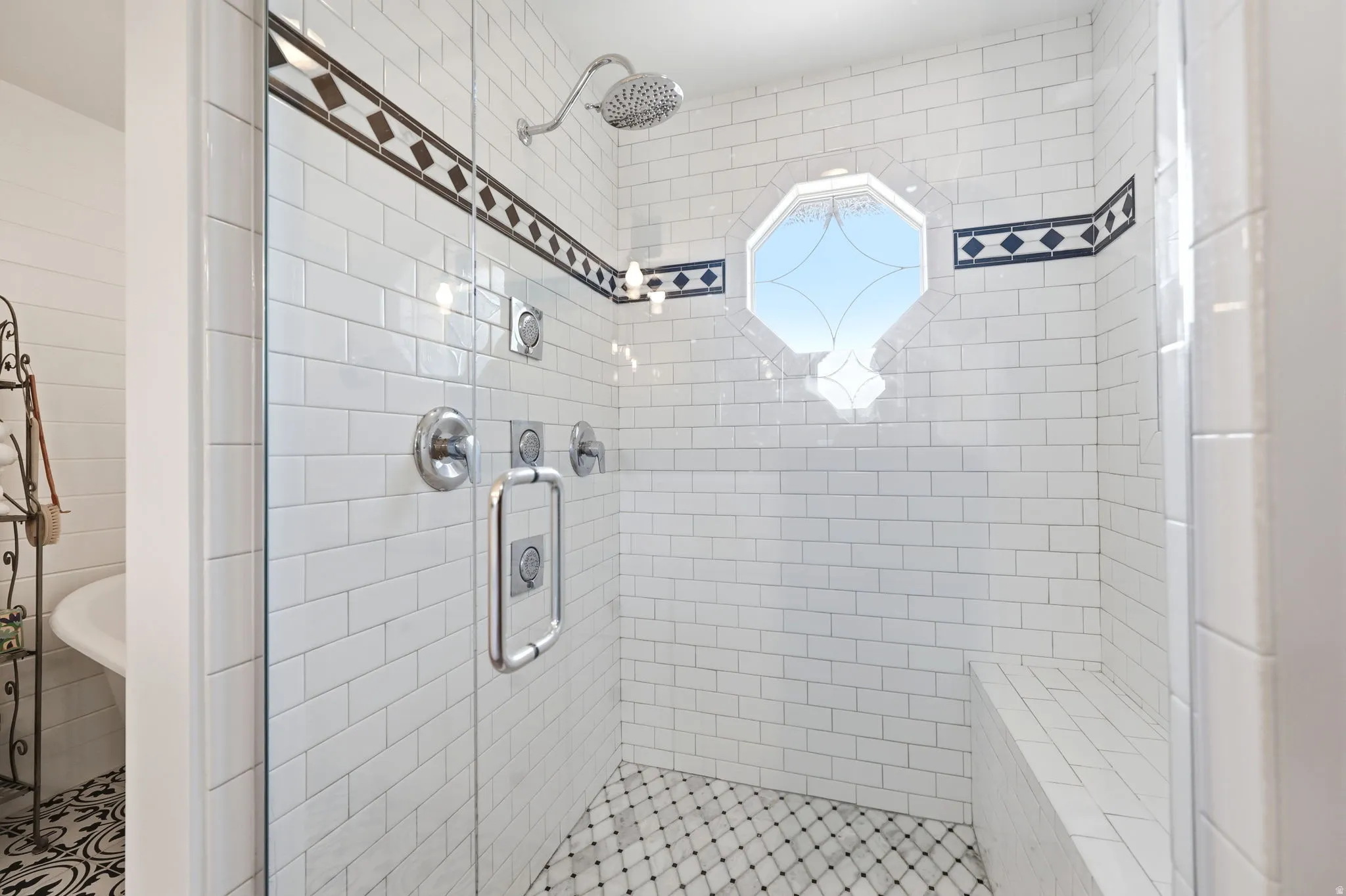 Tiled shower enclosure featuring a frameless glass door, octagonal window, built-in bench, showerhead, and body sprayers