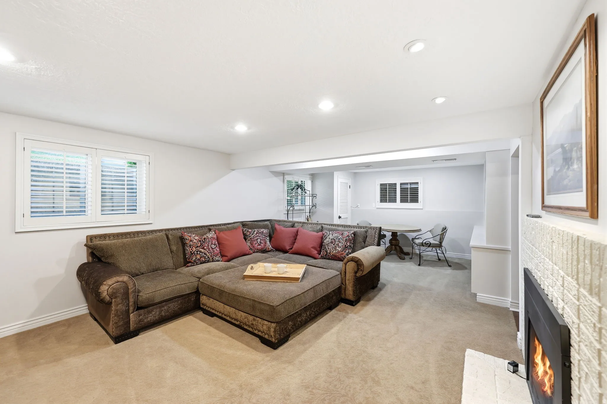 Recessed lighting illuminates this carpeted room featuring a fireplace with a textured white surround