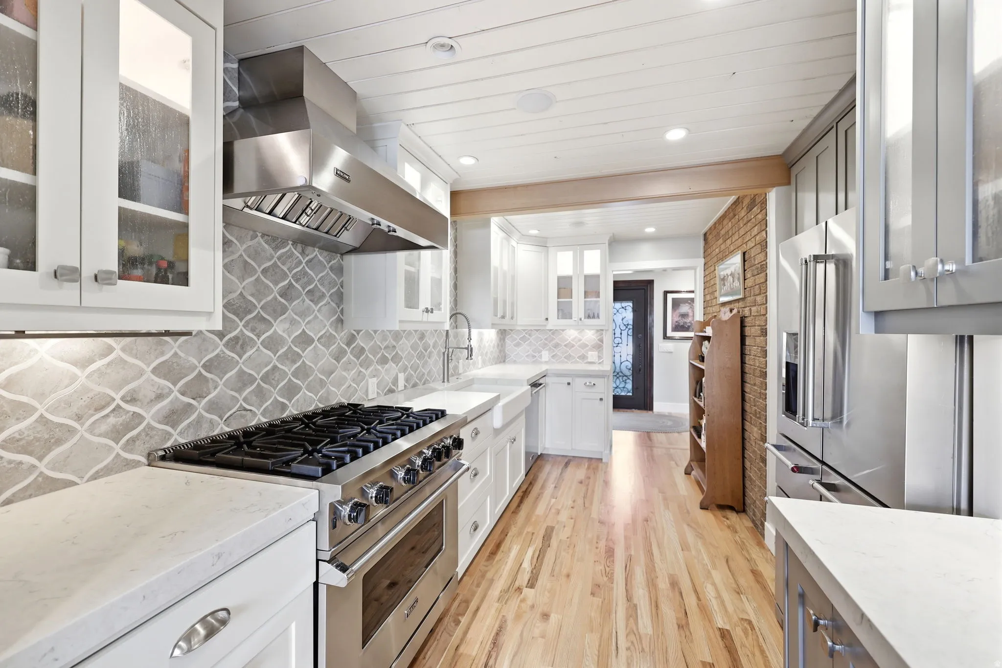 Modern kitchen featuring stainless steel appliances, white cabinetry, a patterned backsplash, light-toned wood-finish flooring, and white countertops