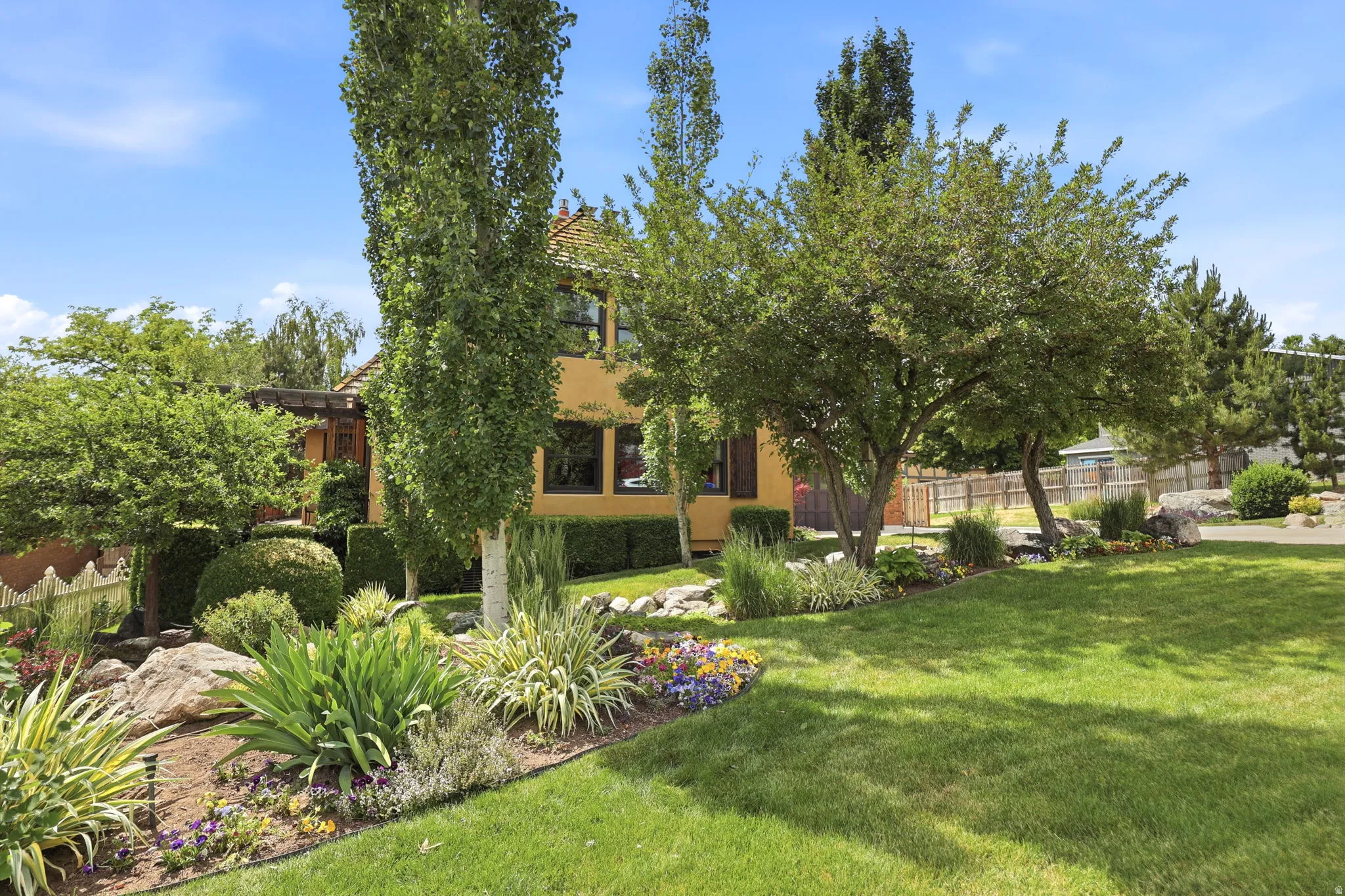 Manicured front yard with expansive lawn, mature trees, ornamental shrubs, natural stone accents, and varied perennial plantings