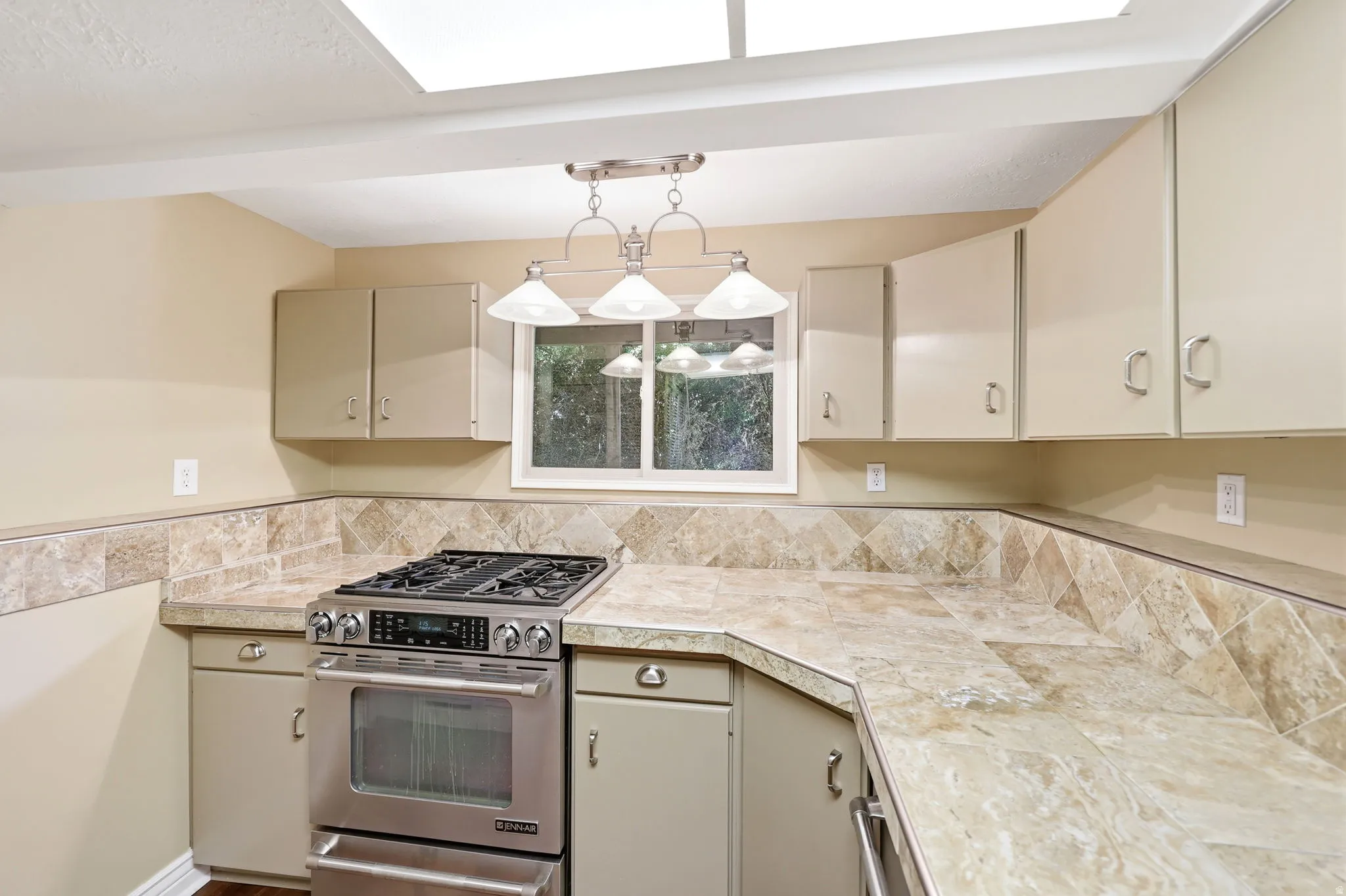 Kitchen featuring an integrated stainless steel range and oven, tile countertops, and a tile backsplash