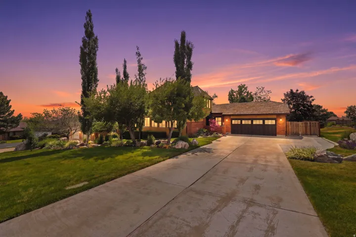 Brick exterior home featuring a concrete driveway, attached garage with panel doors, shingled roof, and mature landscaping with large rocks