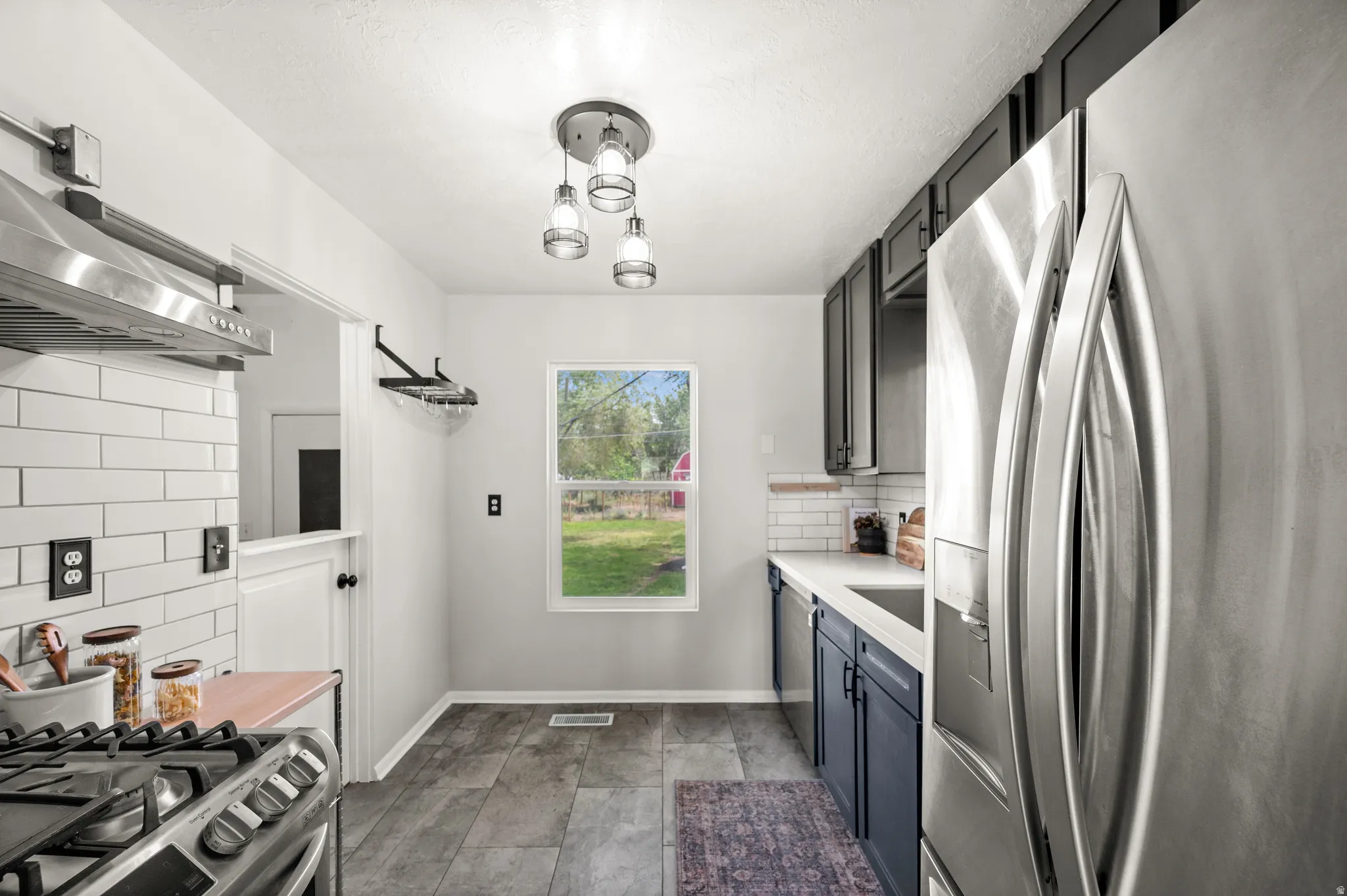 Kitchen featuring wood-finish flooring, two-tone cabinetry, stainless steel appliances, white subway tile backsplash, and a modern pendant light fixture