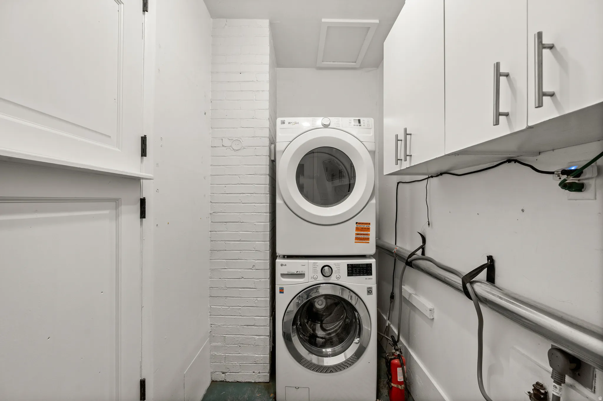 Dedicated laundry area featuring a stacked washer and dryer, white panel cabinetry, white upper storage cabinets with brushed nickel hardware, and painted brick accents