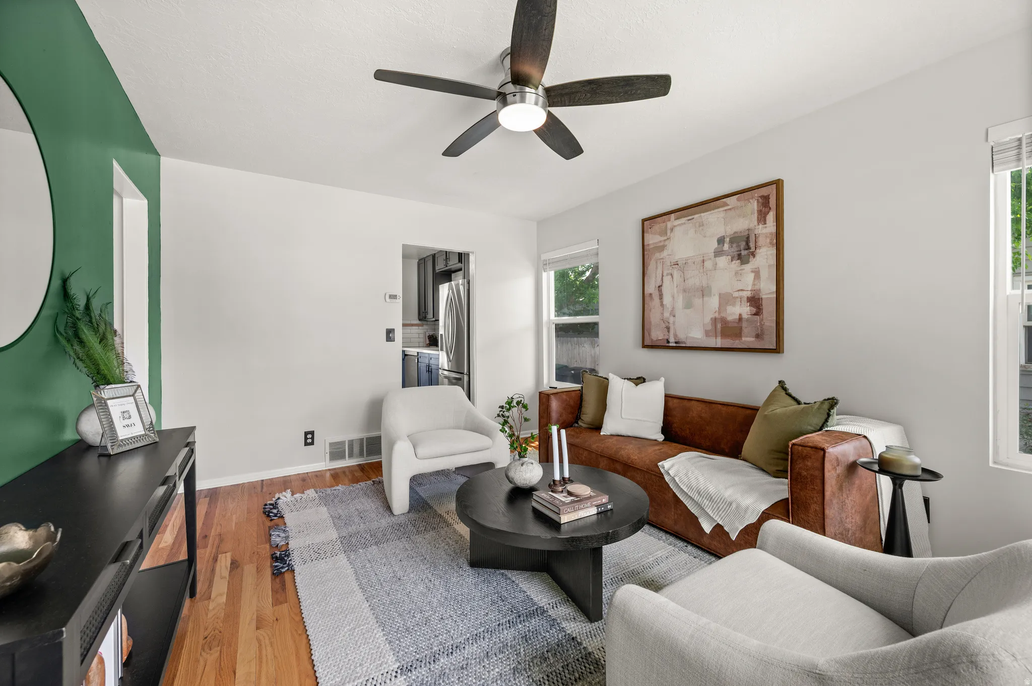 Open concept living area featuring wood-finish flooring, a ceiling fan with integrated lighting, and multiple windows