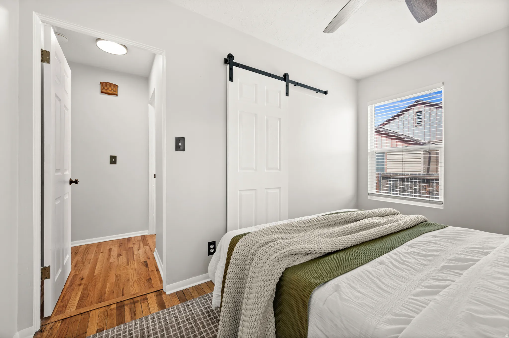Bedroom featuring a single window with blinds, a ceiling fan, and a white sliding barn door