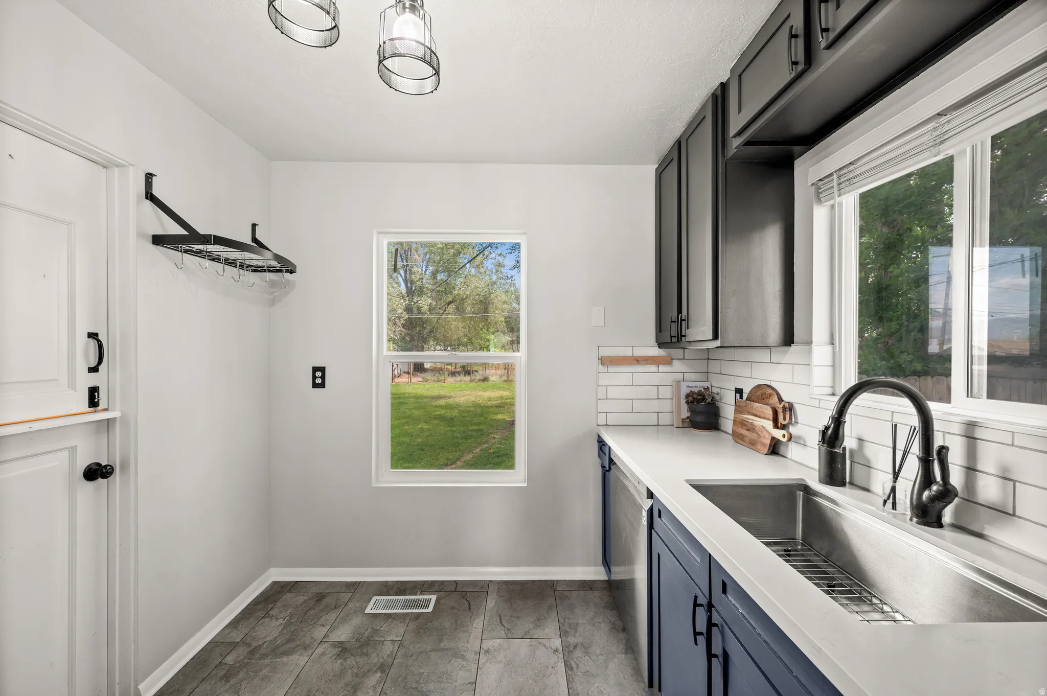 Kitchen featuring blue lower cabinetry, dark upper cabinetry, light countertops, a stainless steel sink with a brushed bronze faucet, and white subway tile backsplash