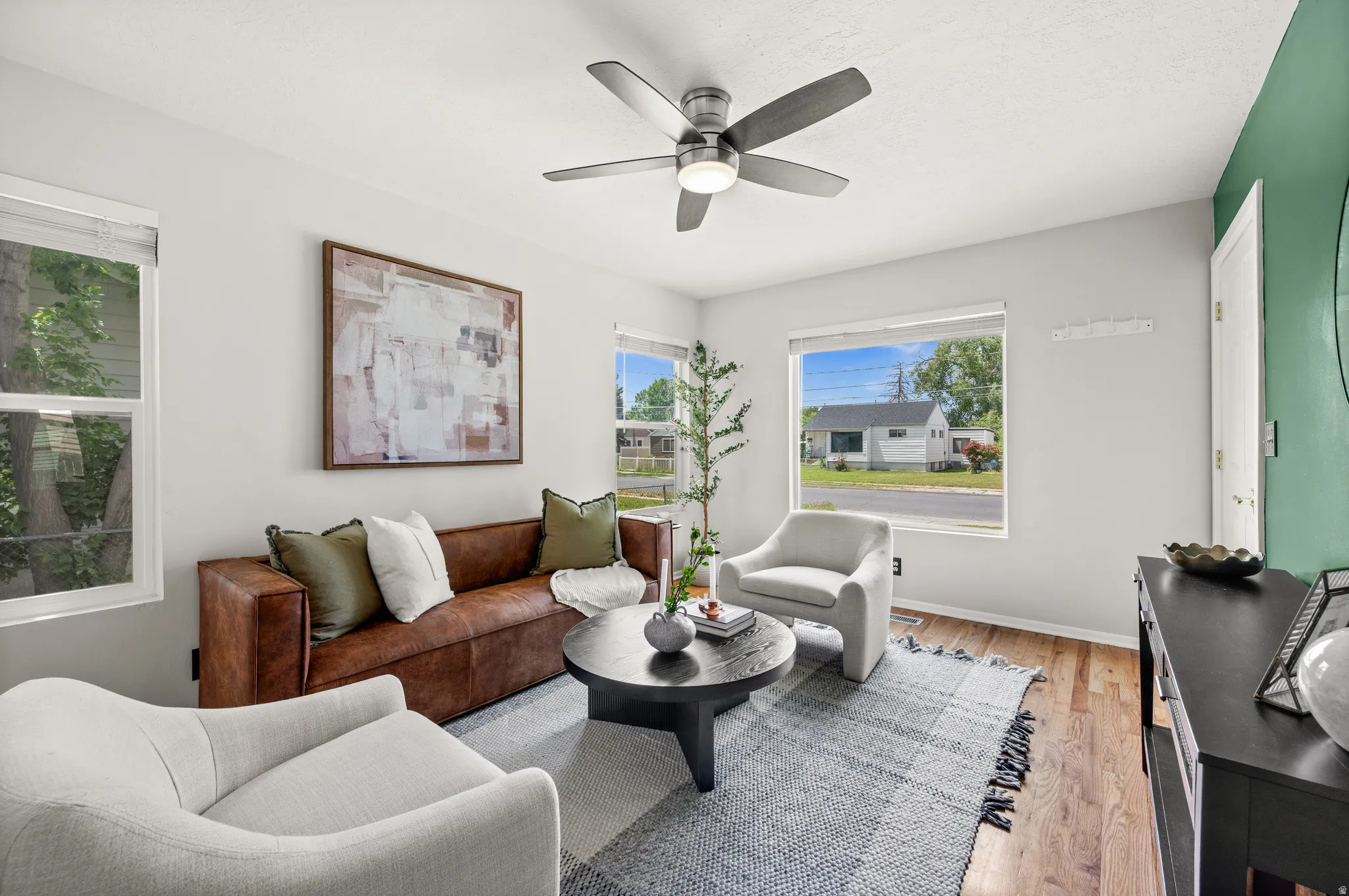 Spacious living area featuring warm wood flooring, crisp white walls, and abundant natural light from multiple windows