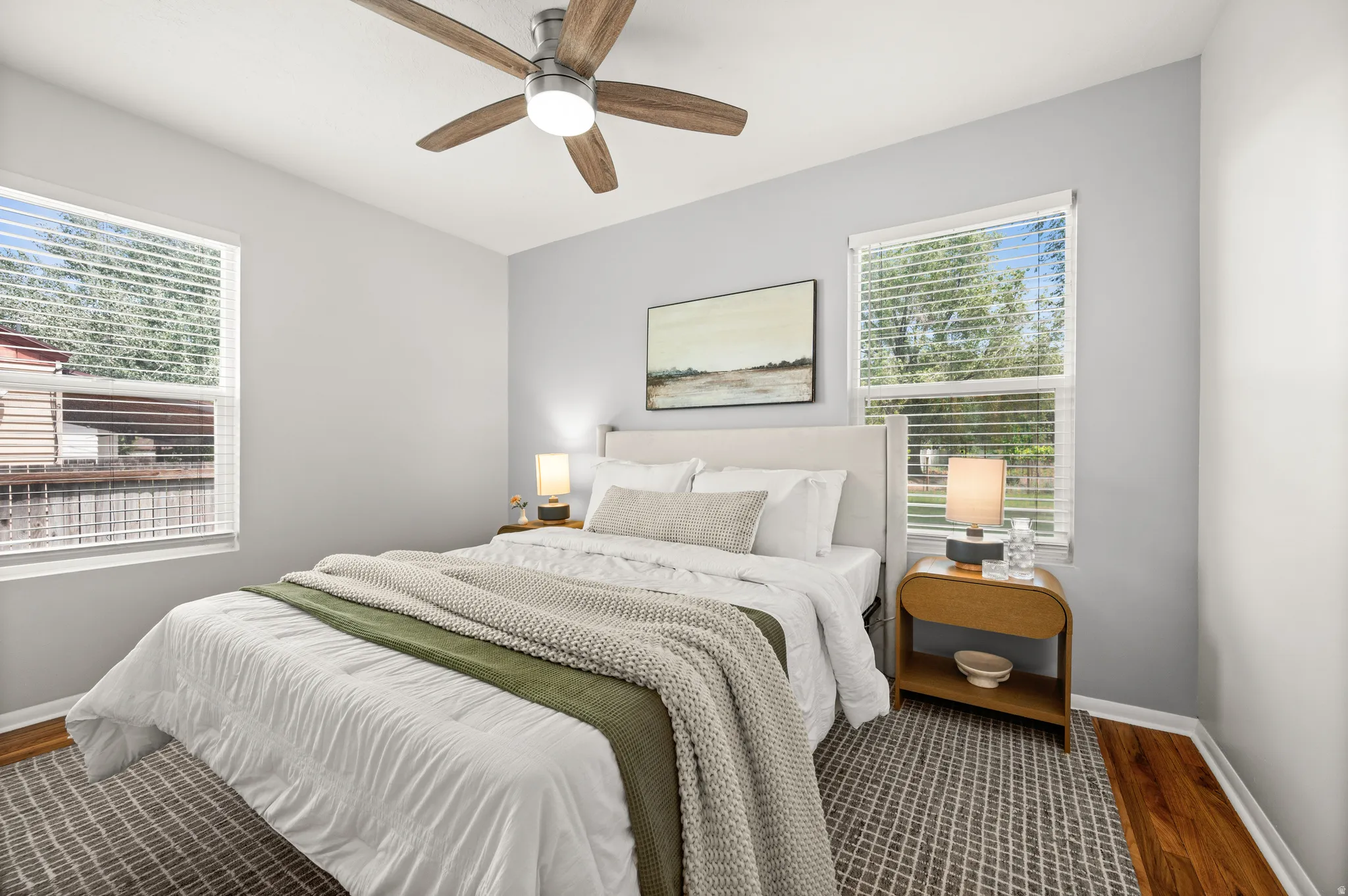 Spacious room featuring two windows with white blinds, light gray walls, a ceiling fan with light fixture, and wood-finish flooring