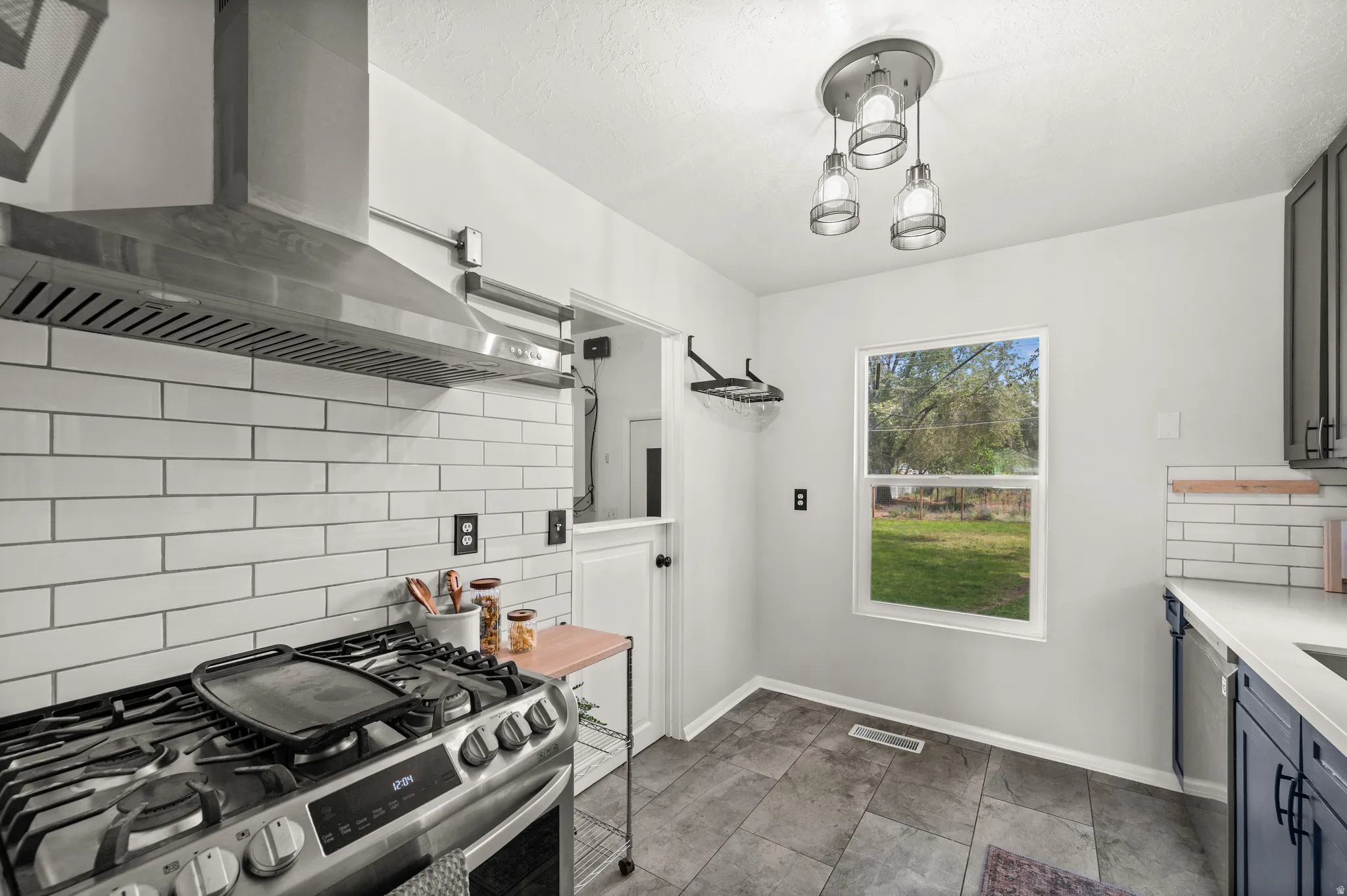 Kitchen featuring a stainless steel range with a coordinating range hood, white subway tile backsplash, dark cabinetry, a white countertop, and gray tile flooring