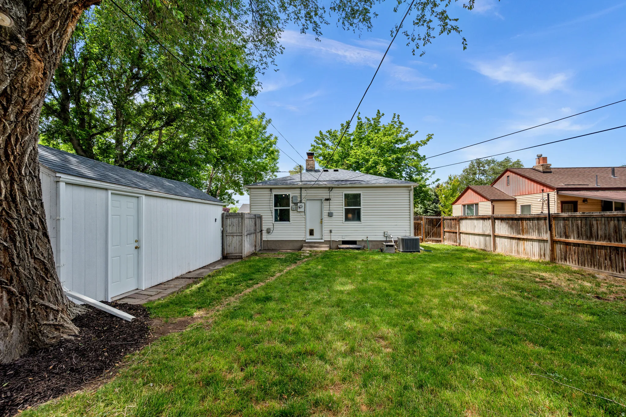 Expansive backyard featuring a green lawn, a white storage shed with a dark roof, and a wood privacy fence