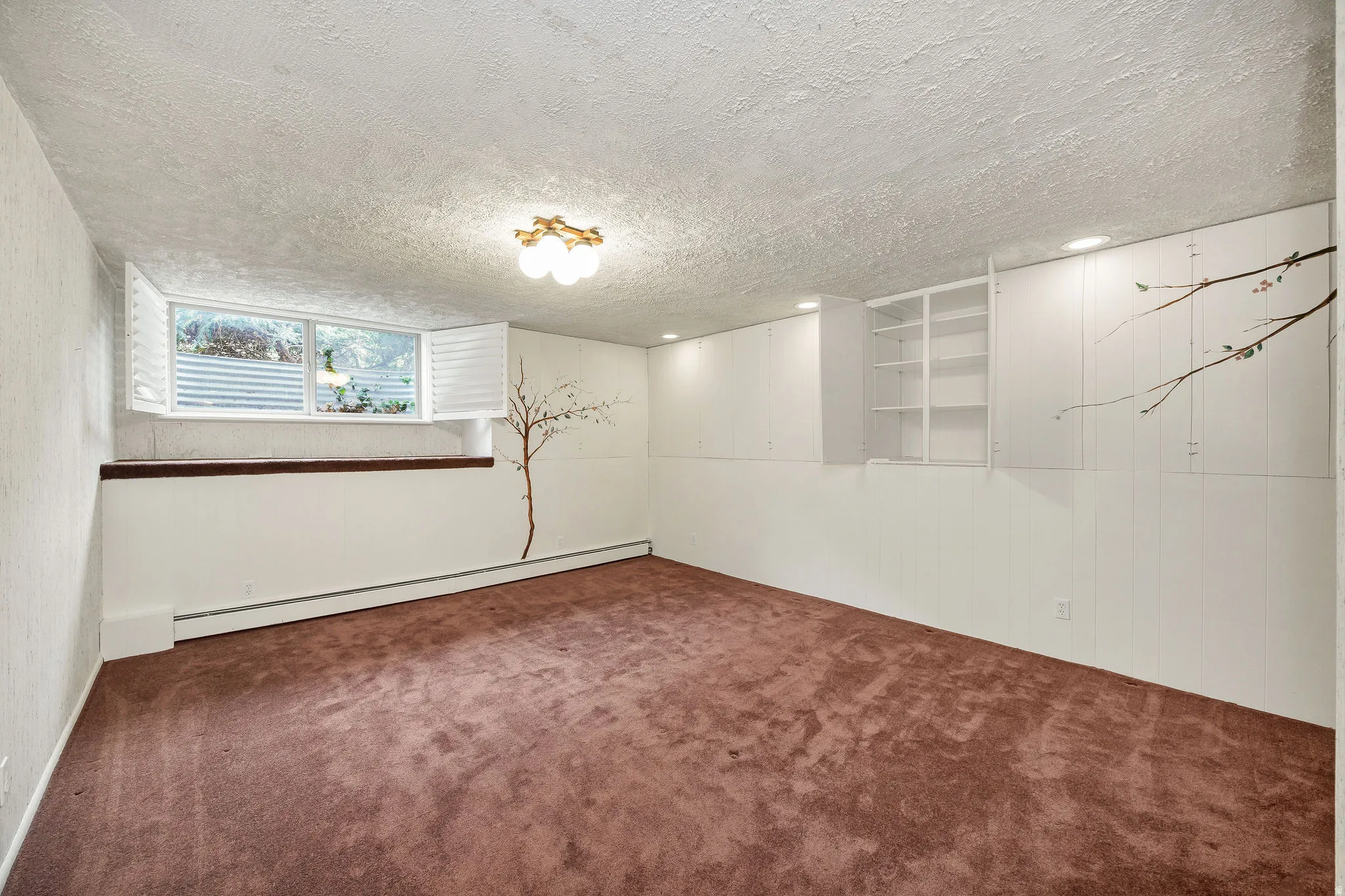 Spacious room featuring brown carpeting, a window with white shutters, a decorative wall decal, built-in cabinetry, and recessed lighting