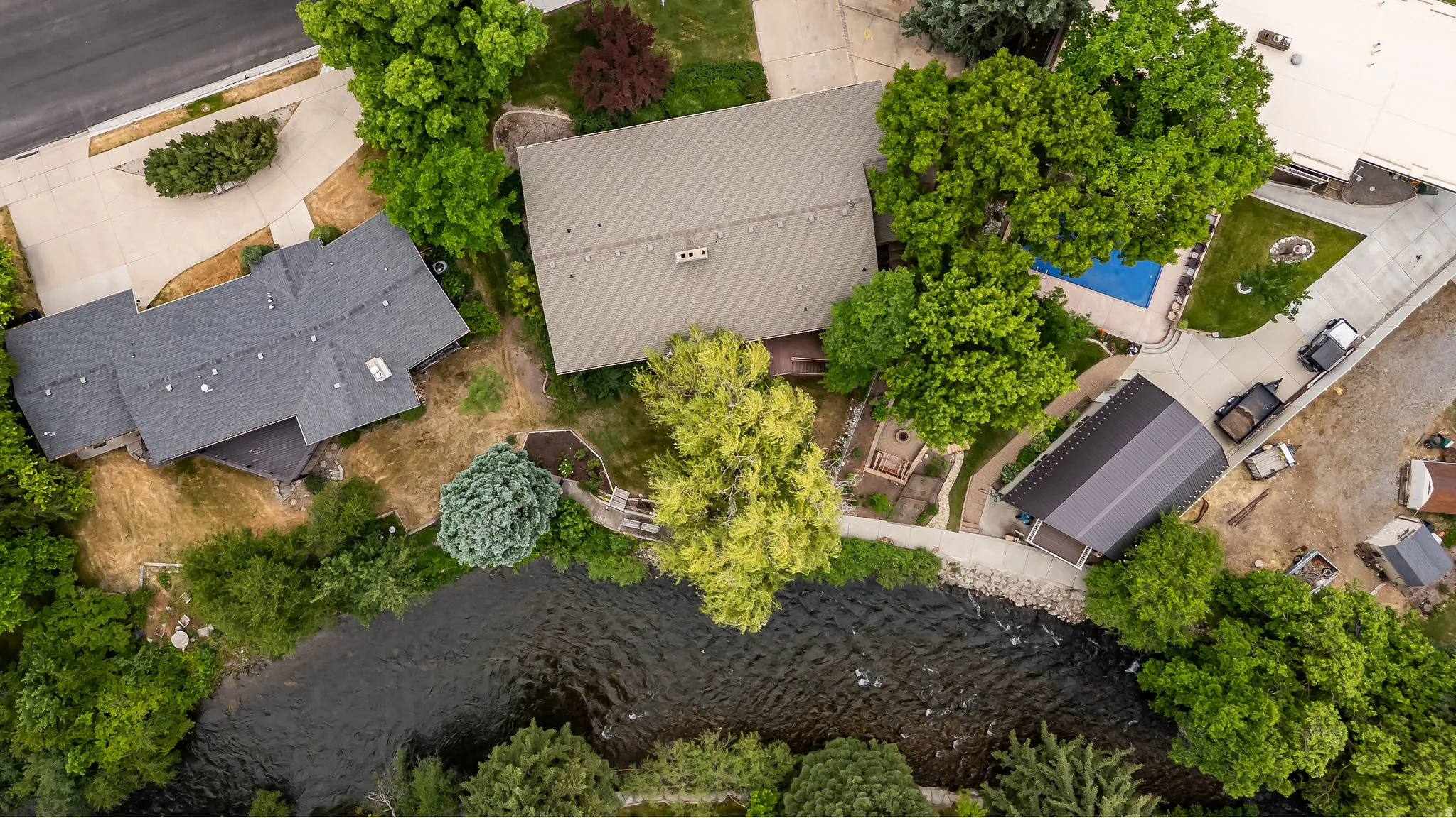 Riverside property featuring a main residence with a gabled roof, an auxiliary structure with a dark metal roof, a pool, and mature trees