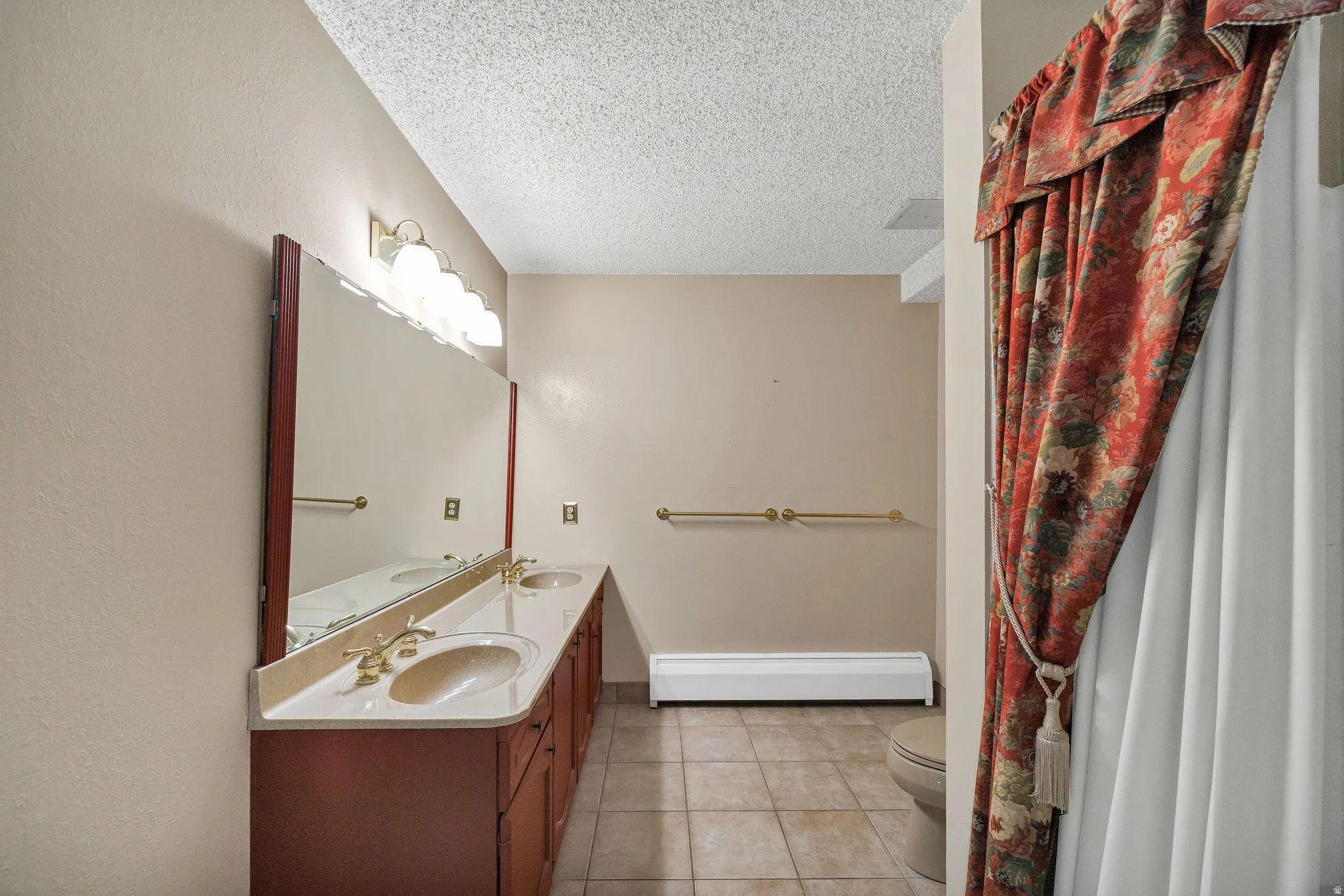 Bathroom featuring a double vanity with integrated sinks, a lengthy mirror, overhead light fixture, and tile flooring