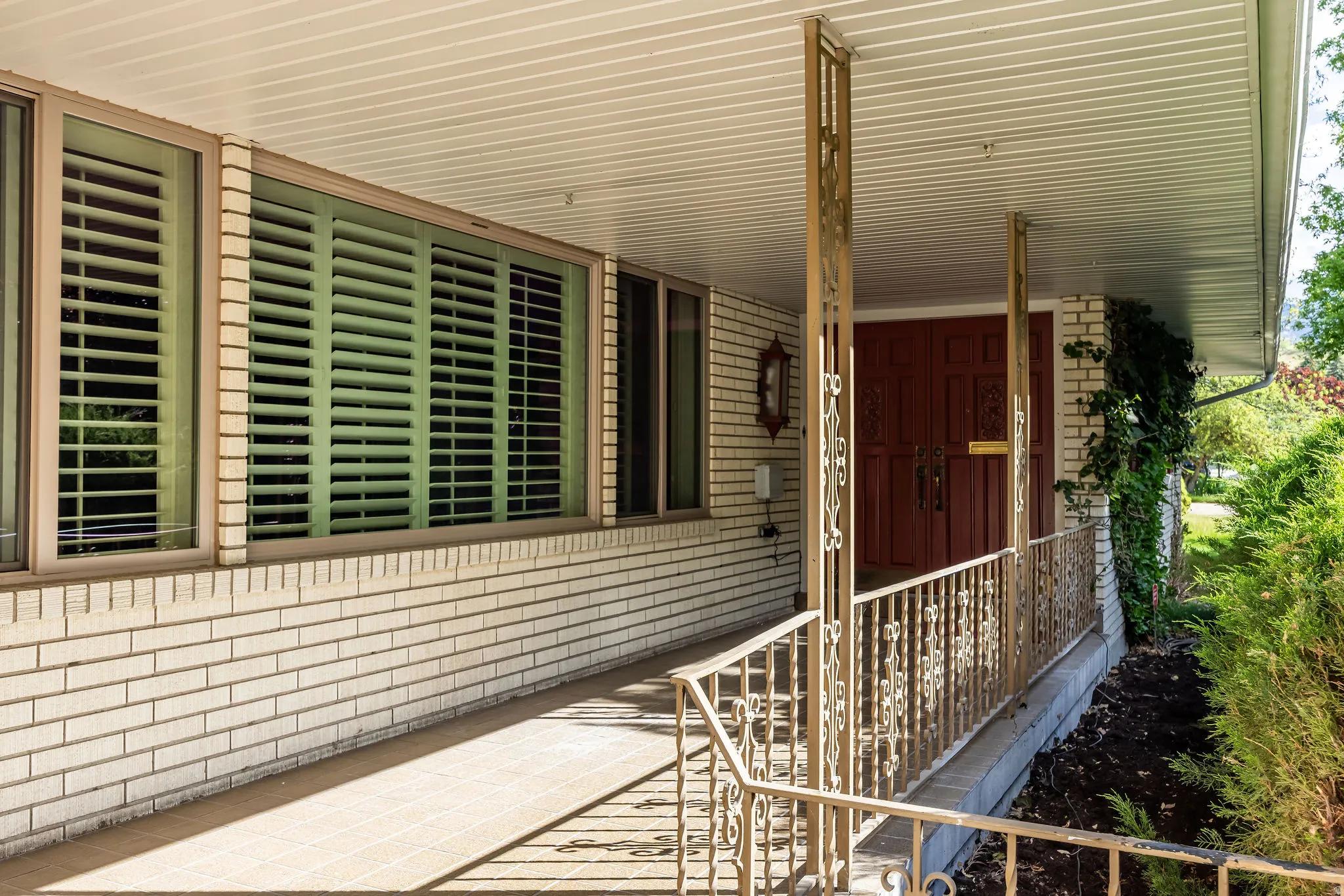 Covered front porch featuring white brick siding, a paneled ceiling, and decorative metal railings