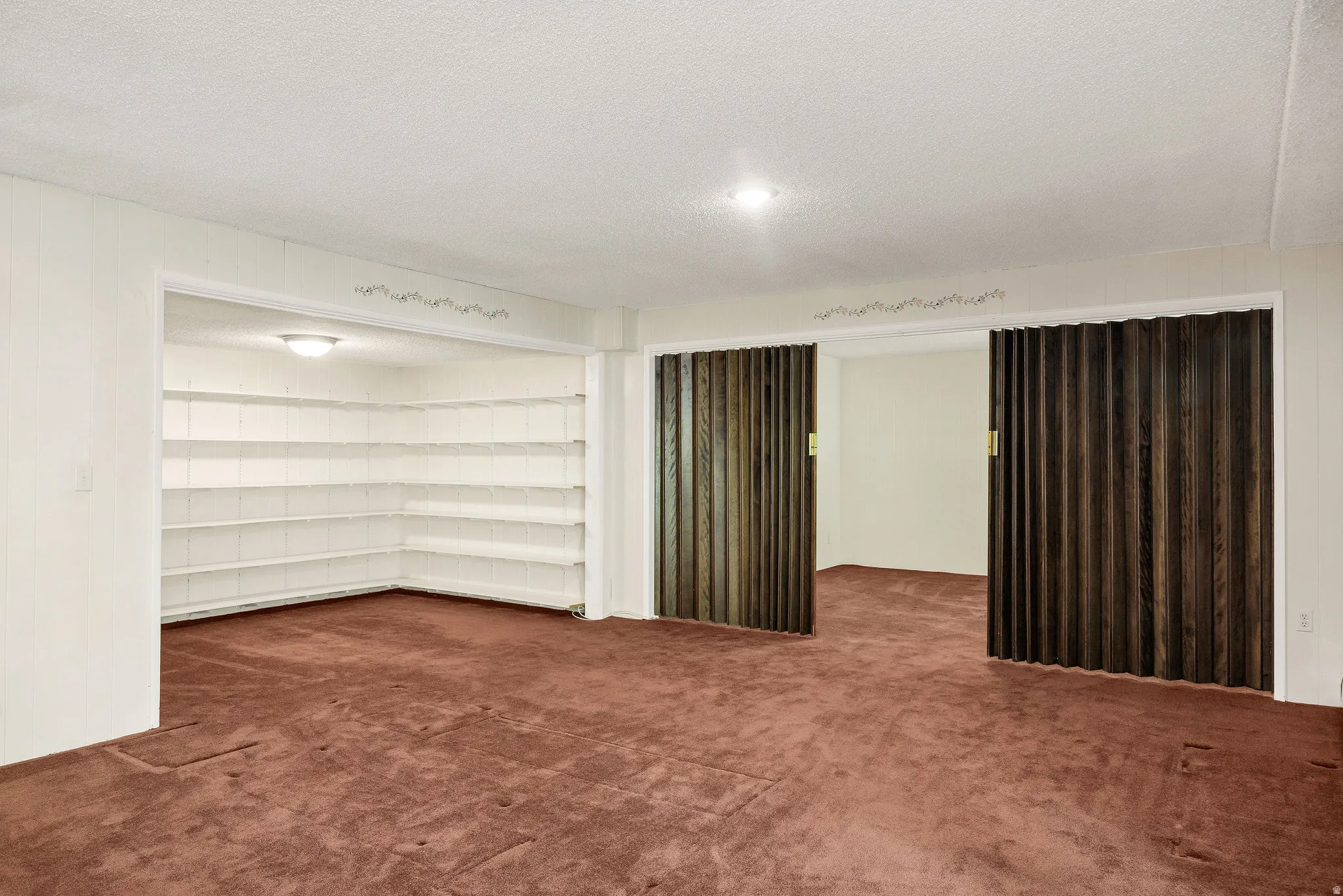Spacious room with plush carpeting, featuring built-in shelving, a recessed ceiling light, and bi-fold wood-finish doors