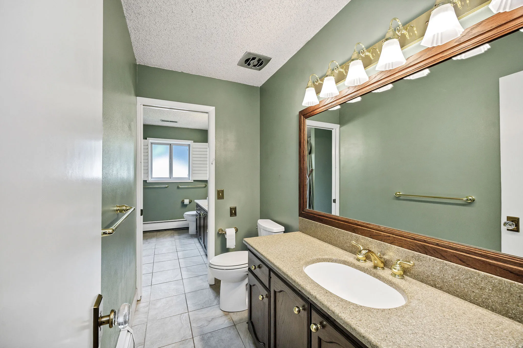 Bathroom vanity featuring a light-toned countertop with integrated sink, wood-framed mirror, and brass-finish fixtures