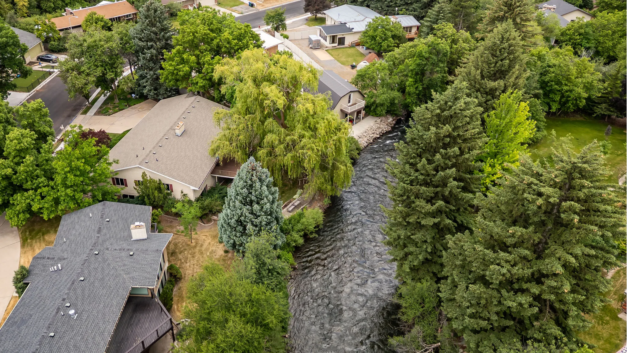 Riverside property featuring a beige-sided residence with a brown roof and a detached outbuilding with a gray metal roof