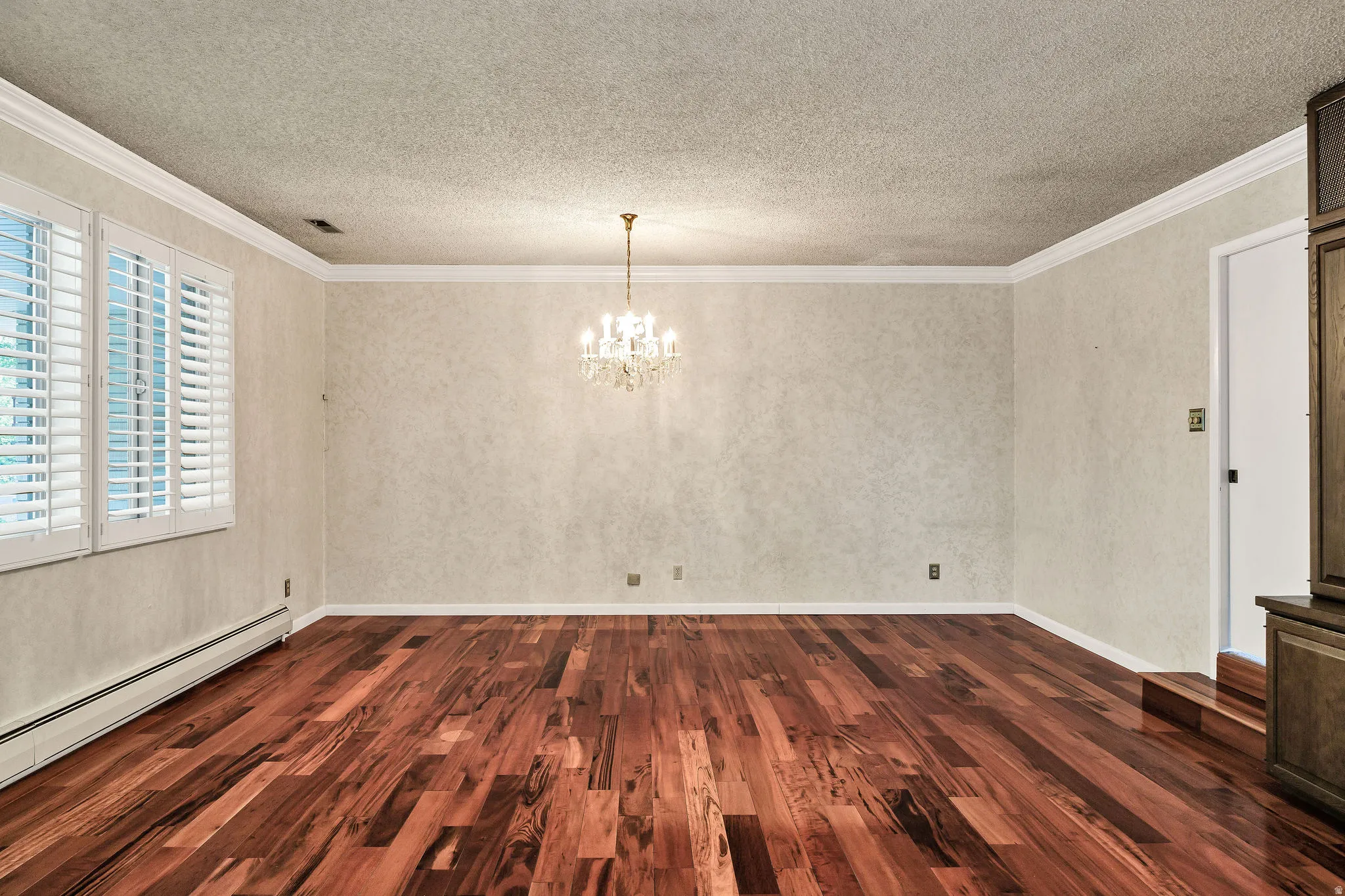 Hardwood flooring throughout featuring white plantation shutters, a crystal chandelier, crown molding, and textured wall coverings