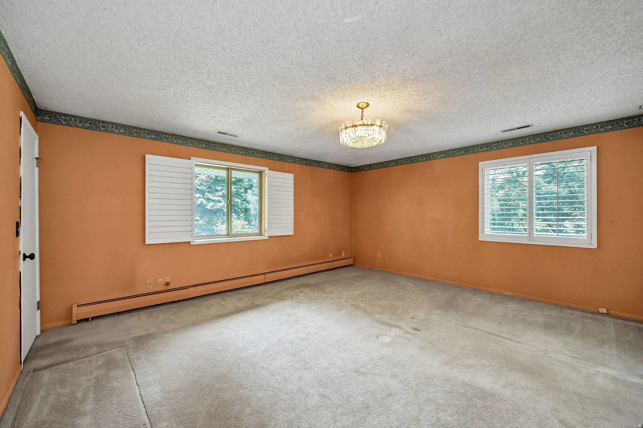 Spacious room featuring two windows with white plantation shutters, a crystal chandelier, and wall-to-wall carpeting